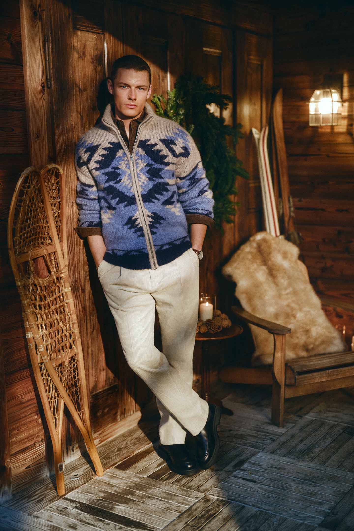 Model styled in a Gant patterned zip-up cardigan paired with corduroy pants in a lodge interior.