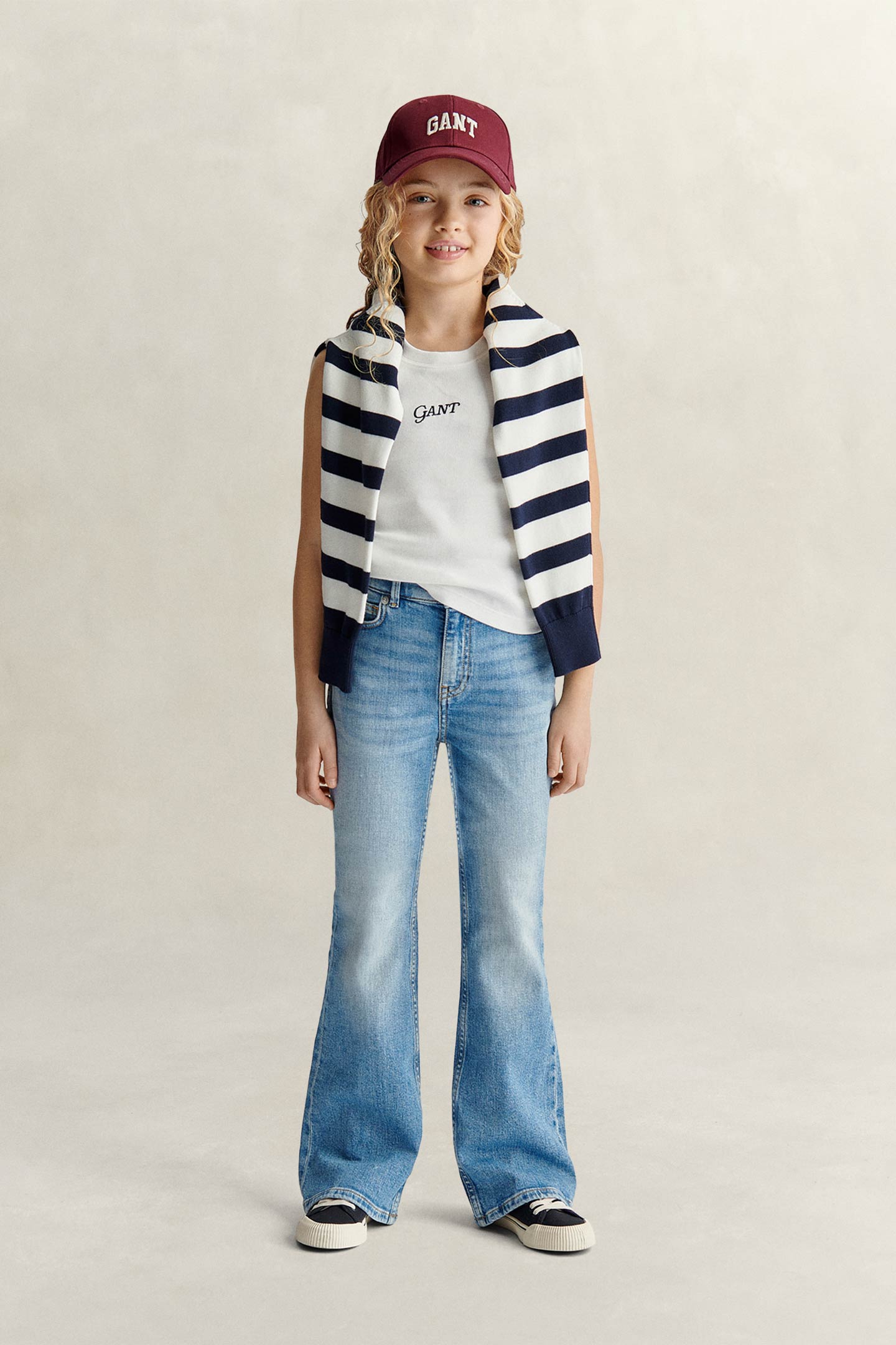 Model styled in a GANT striped knit, tank-top, cap and relaxed denim jeans against a grey backdrop.