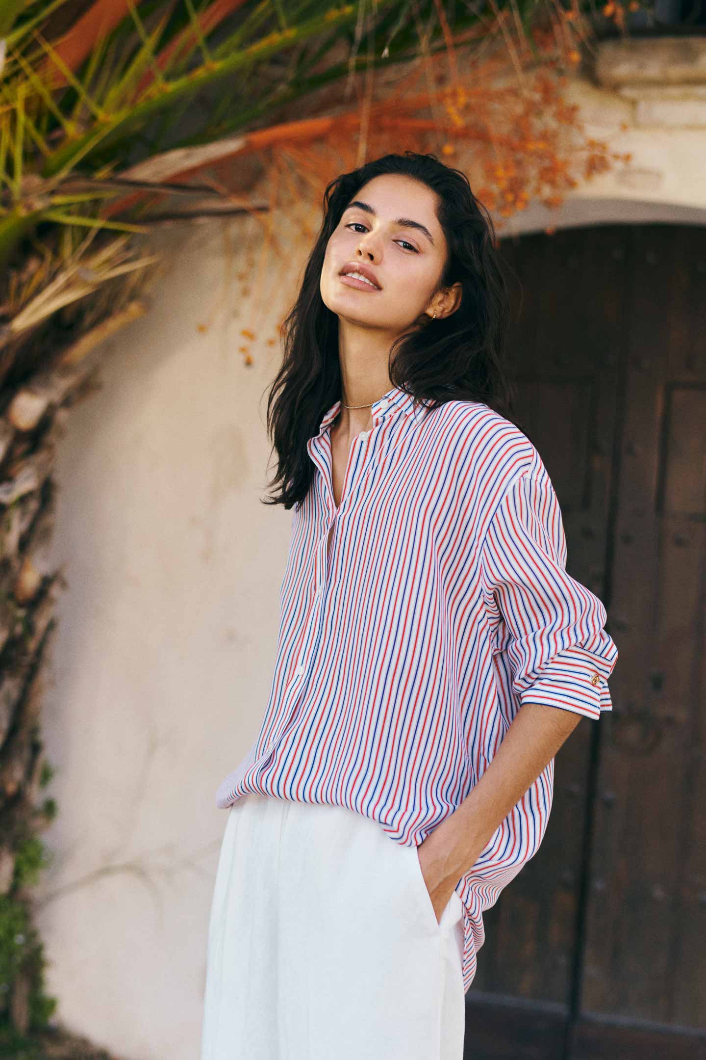 Woman wearing a Gant red and blue striped button-down shirt with white trousers outdoors.