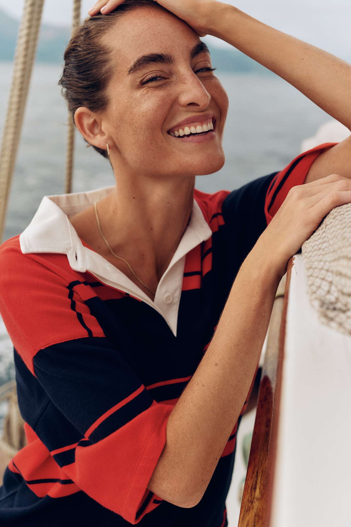 Woman smiling on a boat while wearing a Gant red and navy striped rugby shirt.