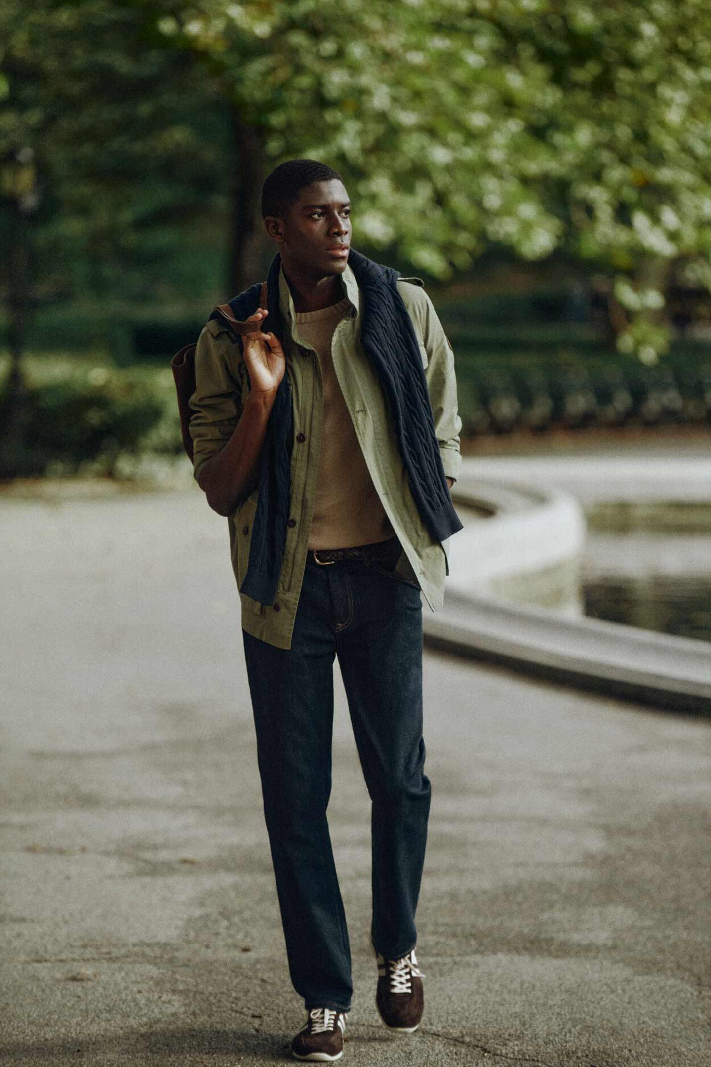 Person walking outdoors wearing a Gant jacket, sweater, polo shirt, dark trousers and sneakers.