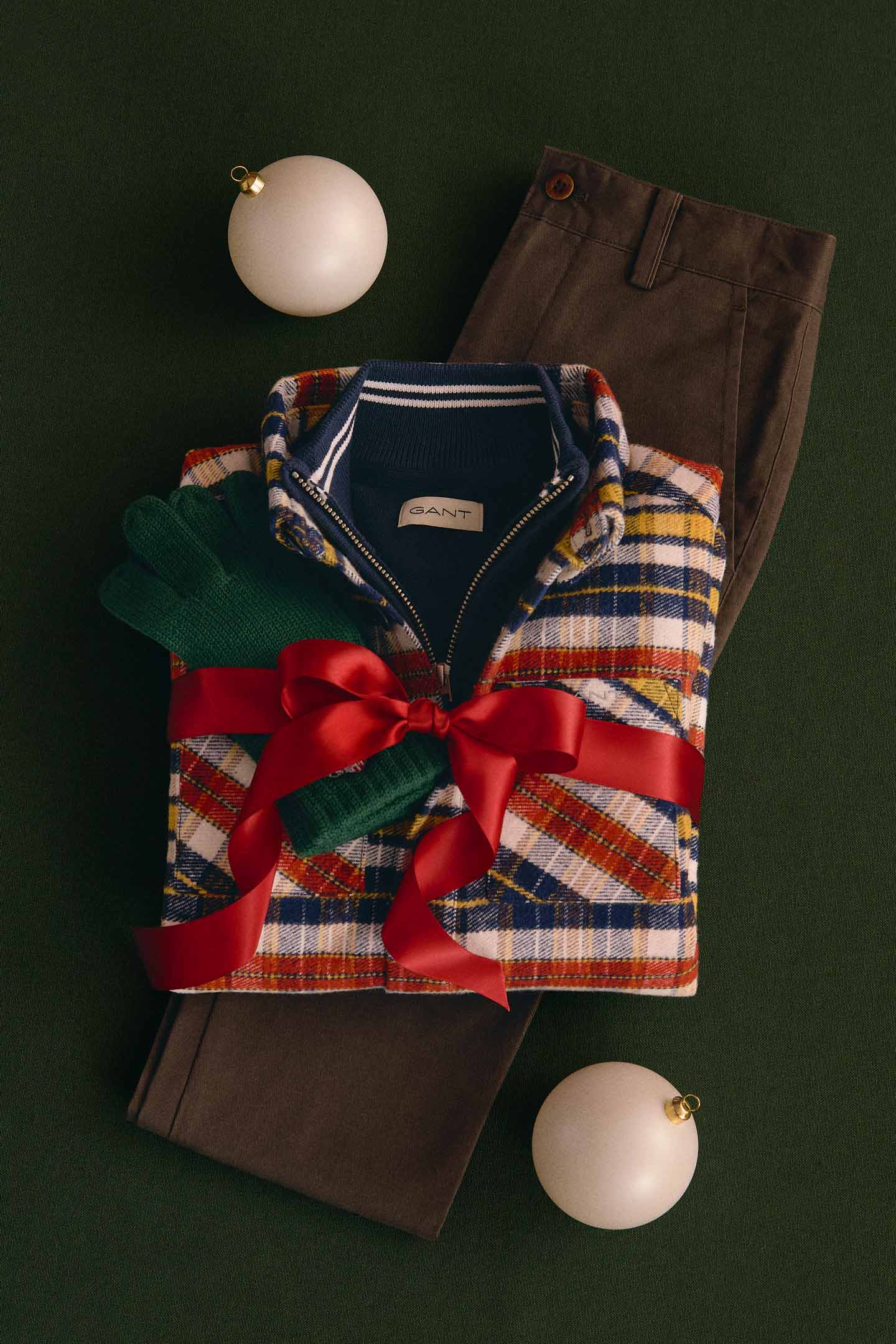 Folded Gant multicolor plaid zip-up overshirt layered over a navy knit top, paired with brown trousers.