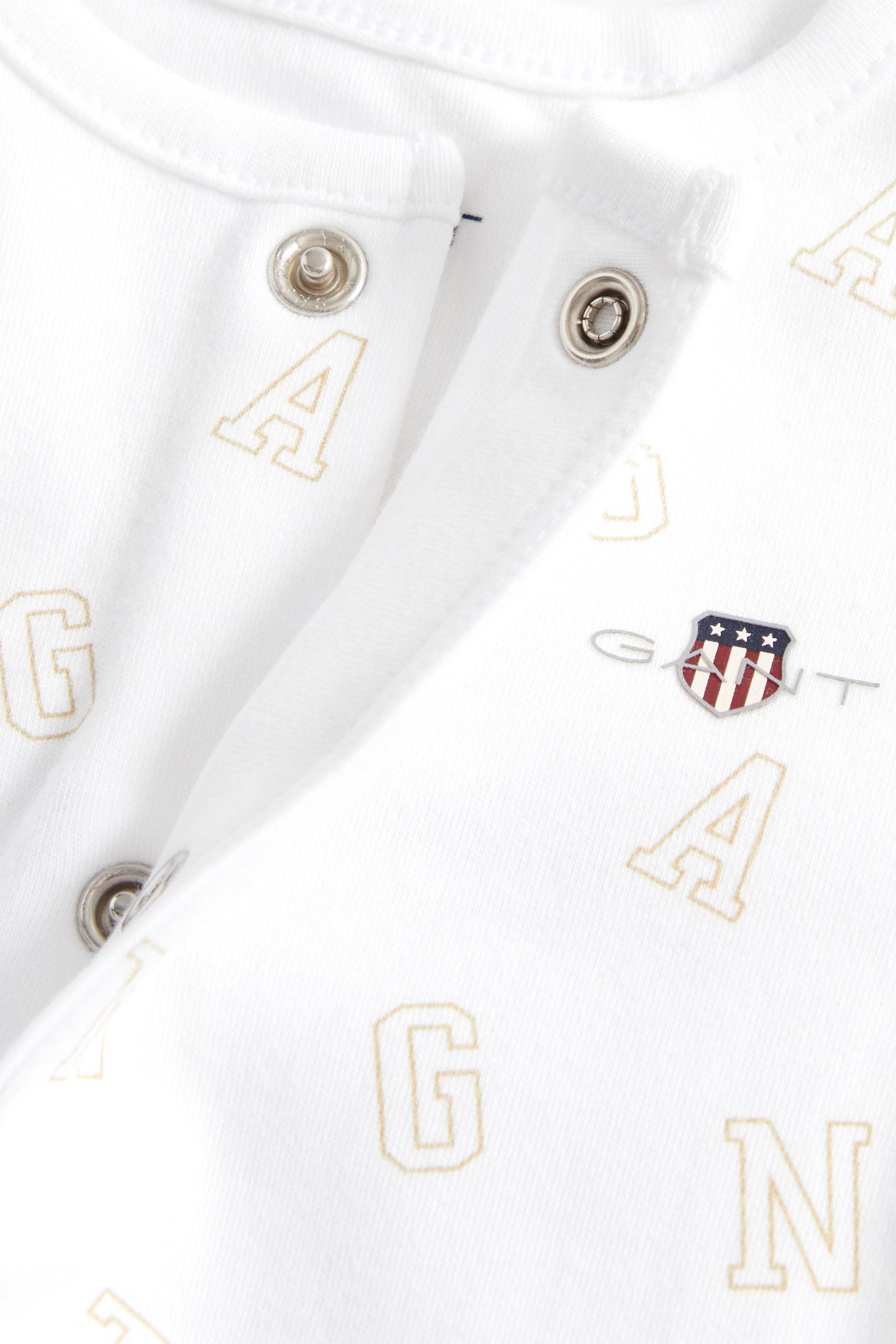 Close-up of a Gant baby bodysuit in white with snap buttons and printed letter pattern.