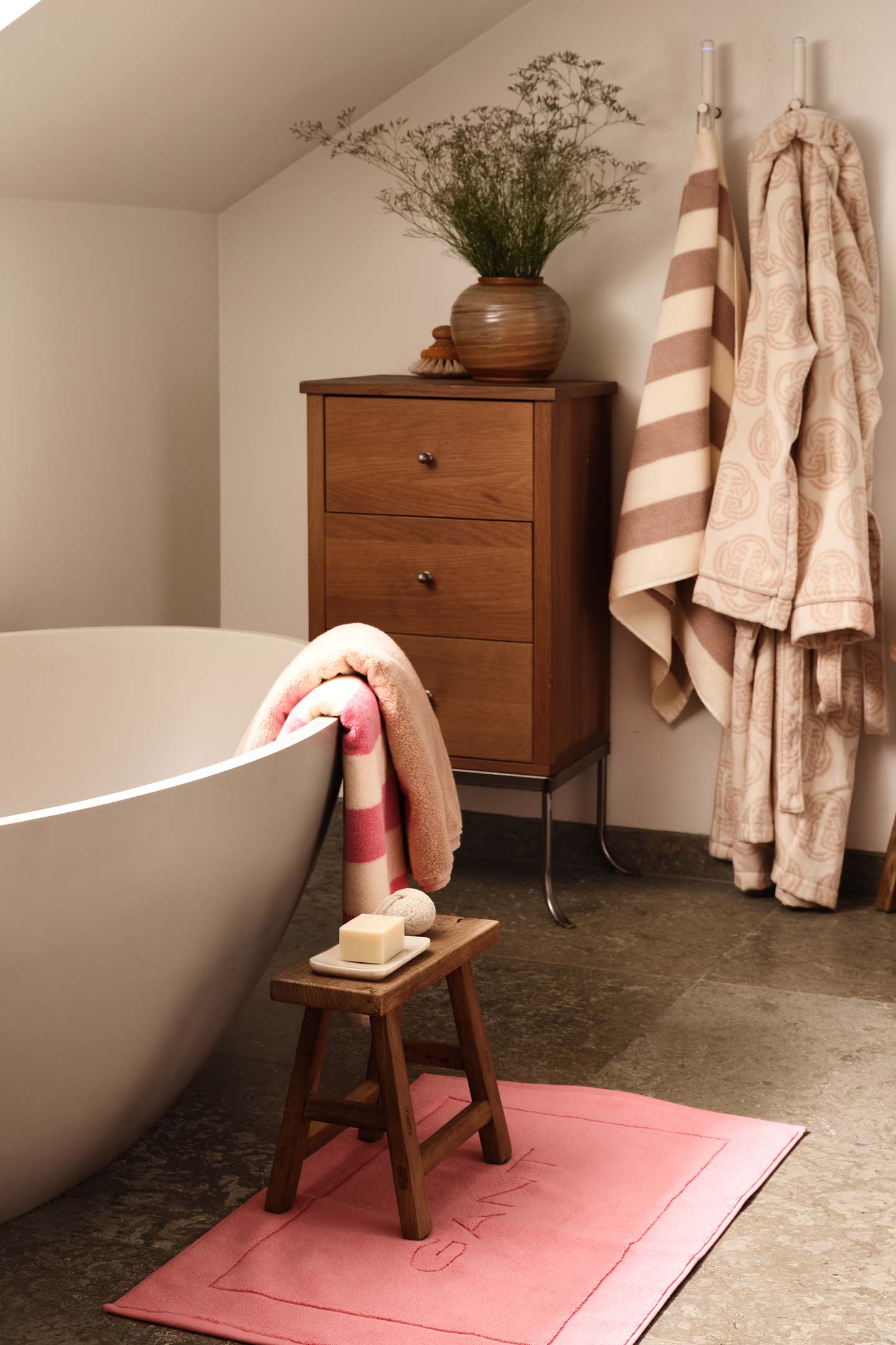 Gant bath towels and bath mat styled beside a freestanding bathtub in a calm bathroom interior.