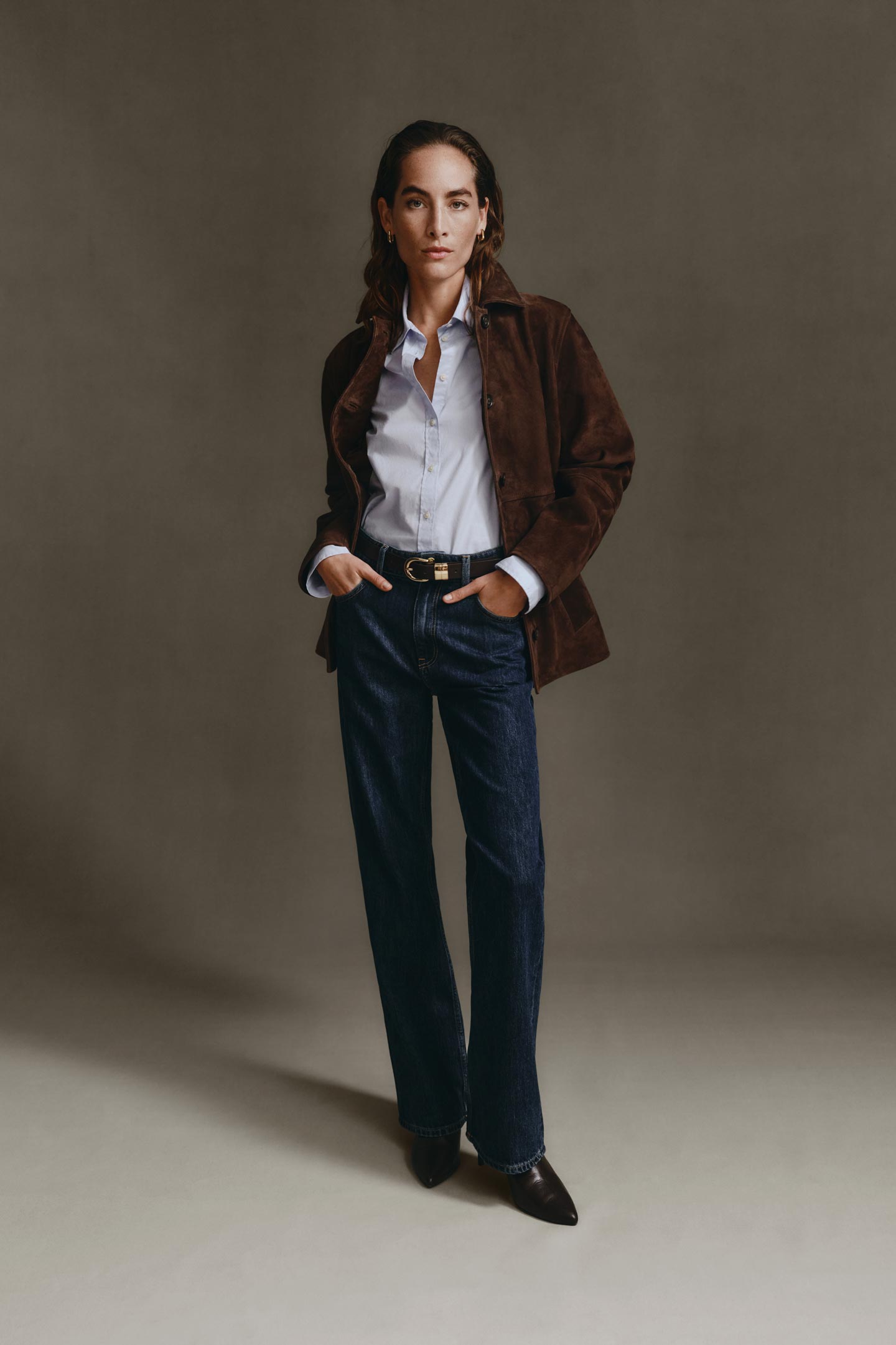 Model styled in a Gant suede jacket worn over a button-down shirt and jeans, standing in a studio setting.