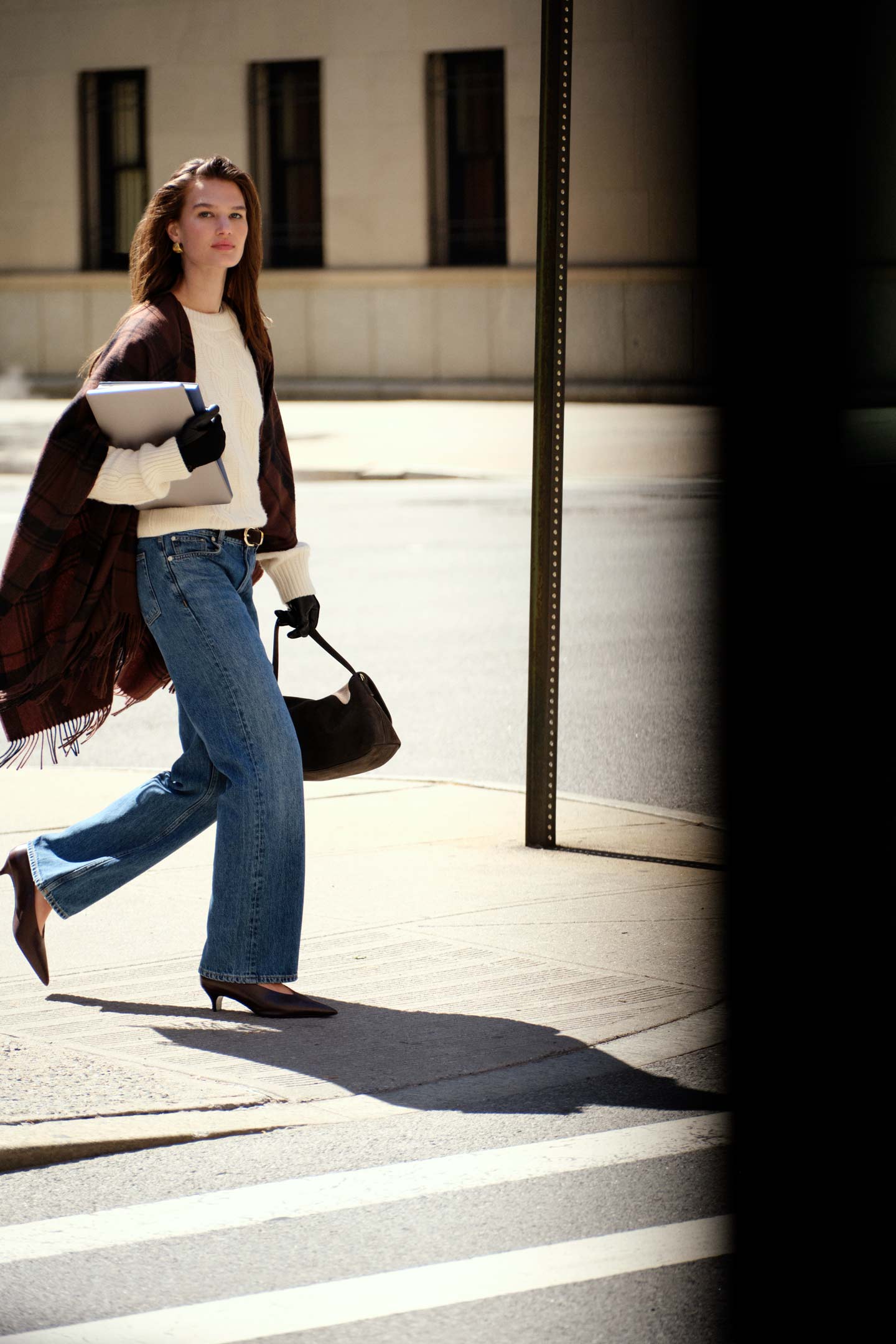 Model styled in a Gant cable-knit sweater worn with jeans and a checked wrap, carrying a shoulder bag and folders.