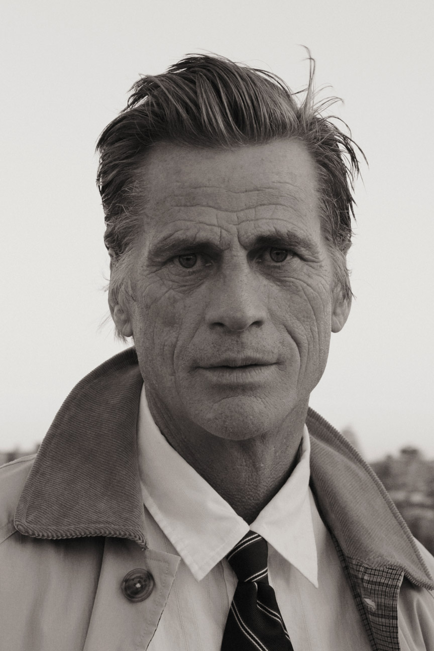Man wearing a Gant trench coat, collared shirt and striped tie in a close-up portrait