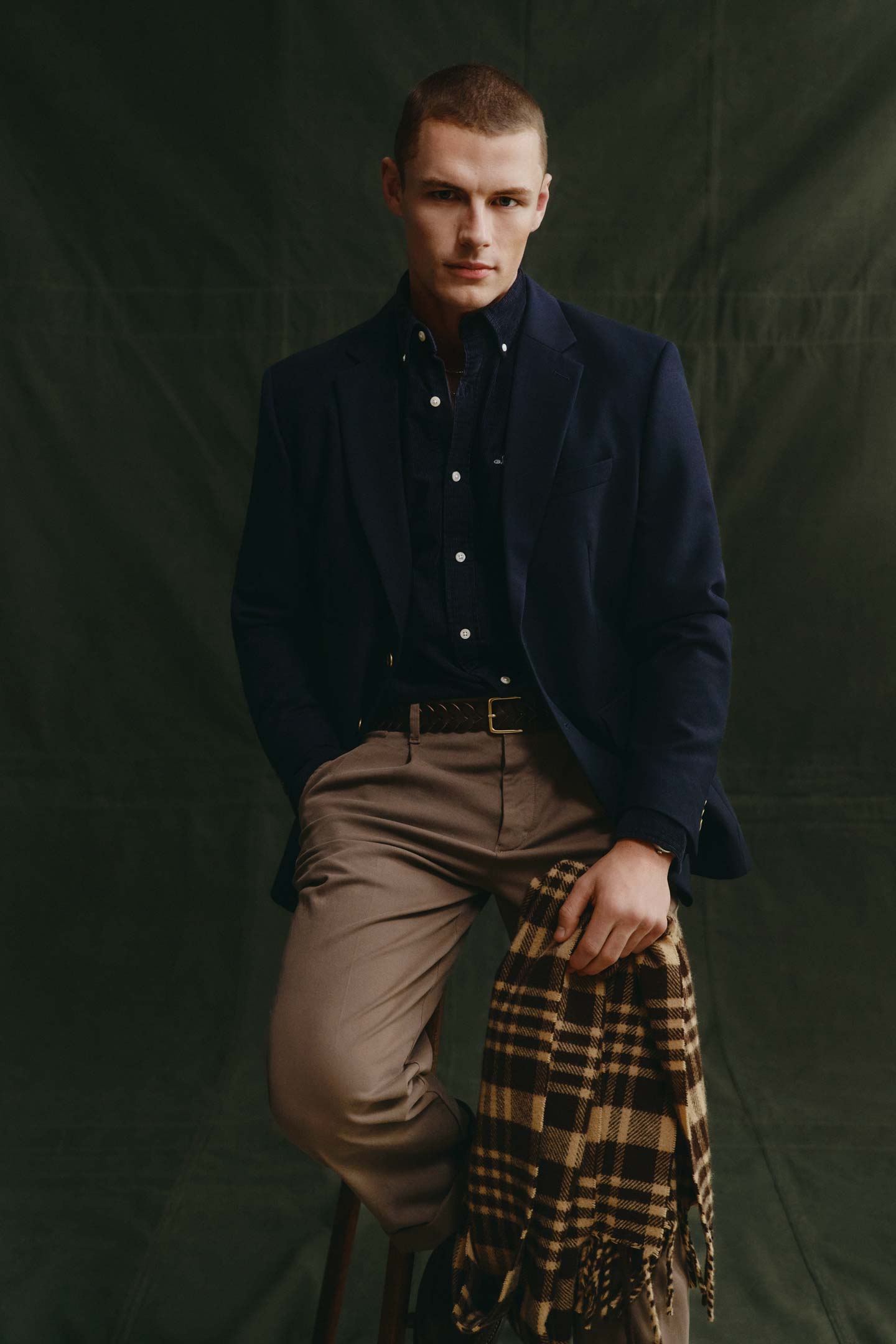 Model styled in a Gant blazer layered over a button-down shirt and tailored pants, holding a checked scarf.