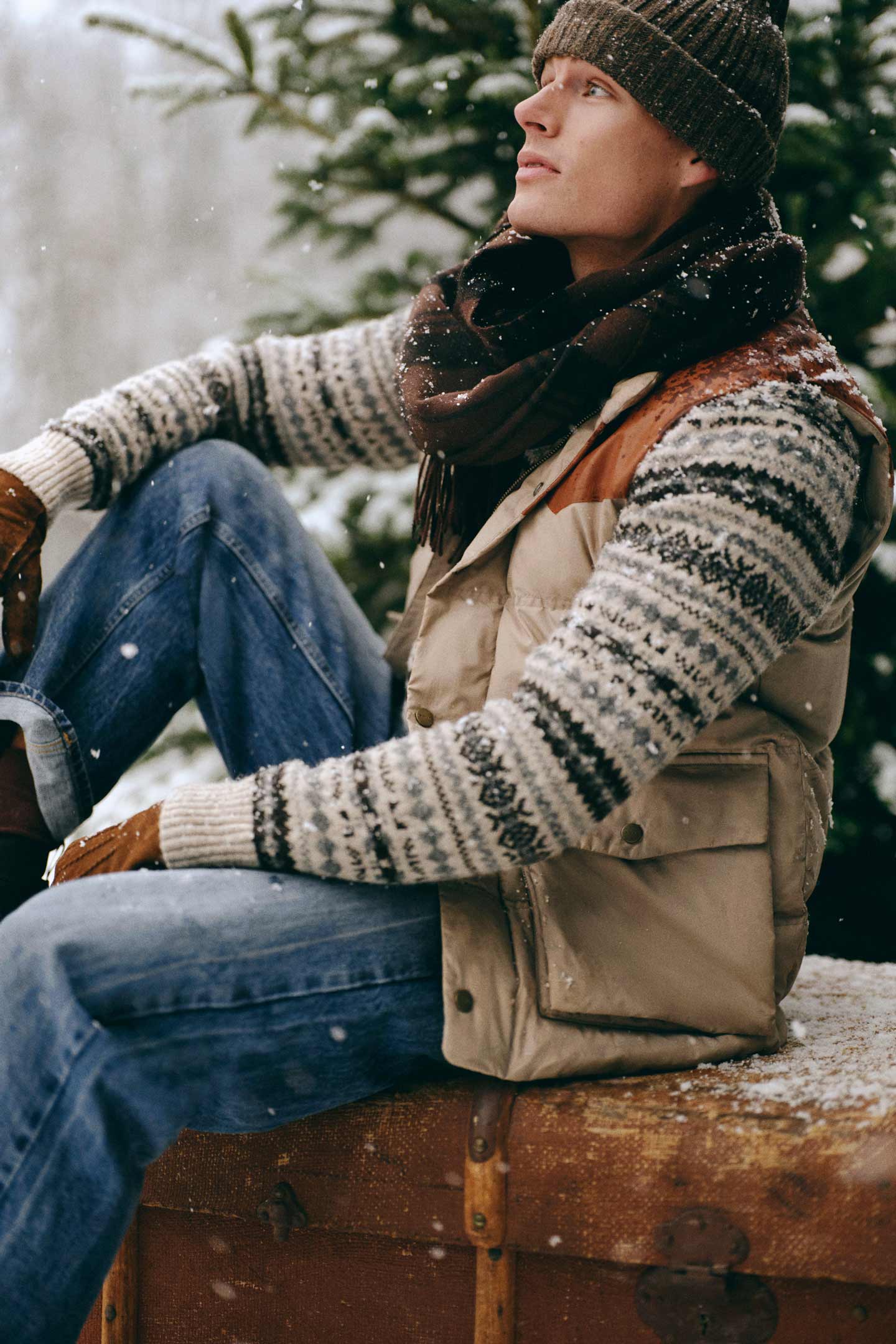 Model styled in a Gant padded vest layered over a patterned knit sweater, jeans, scarf and beanie in the snow.