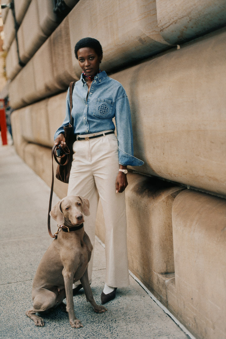 Personne portant une chemise en jean Gant et un pantalon clair, debout près d’un mur avec un chien.