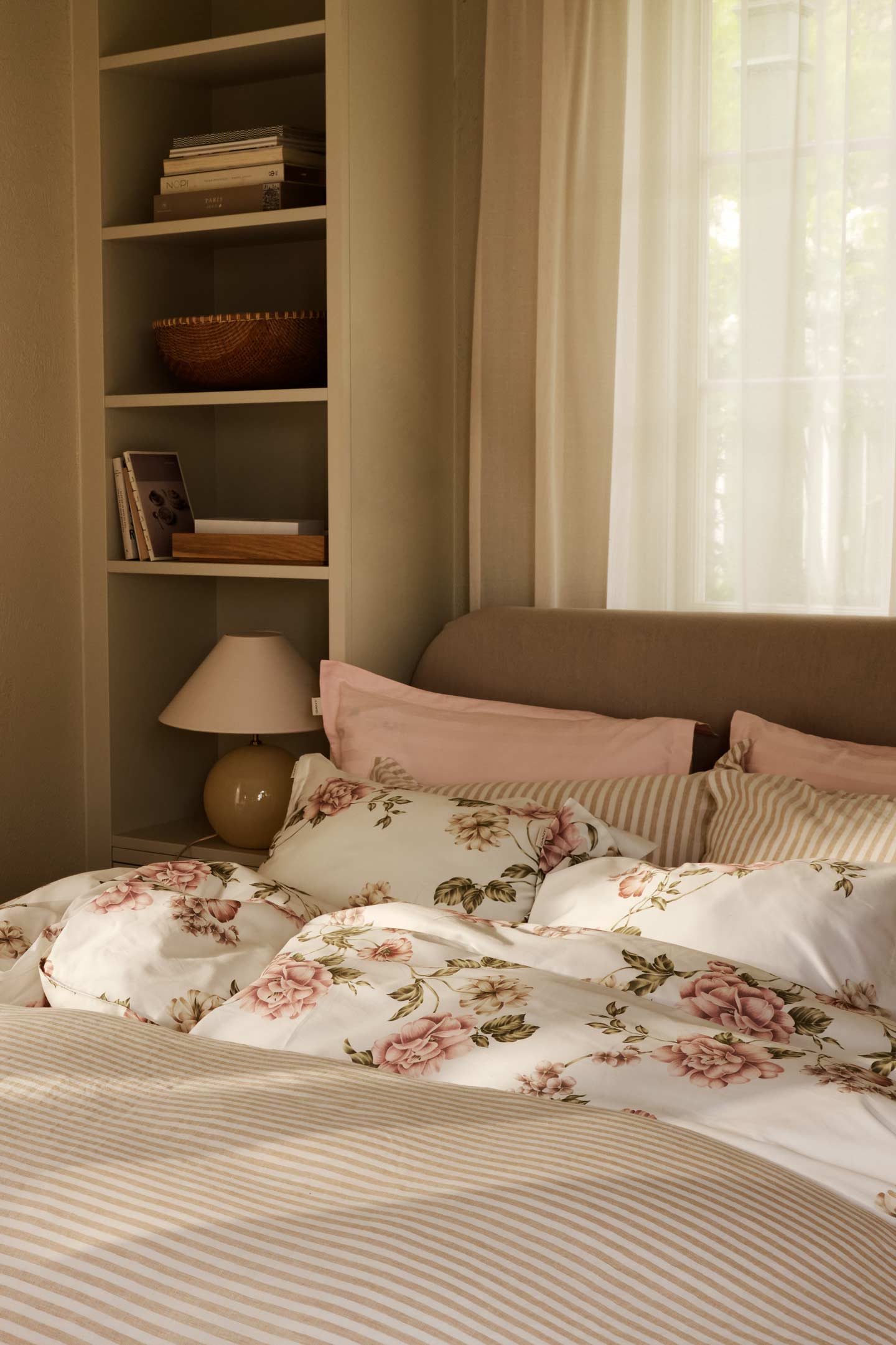 Gant bedding set with striped and floral duvet and pillows arranged on a bed in a softly lit bedroom.