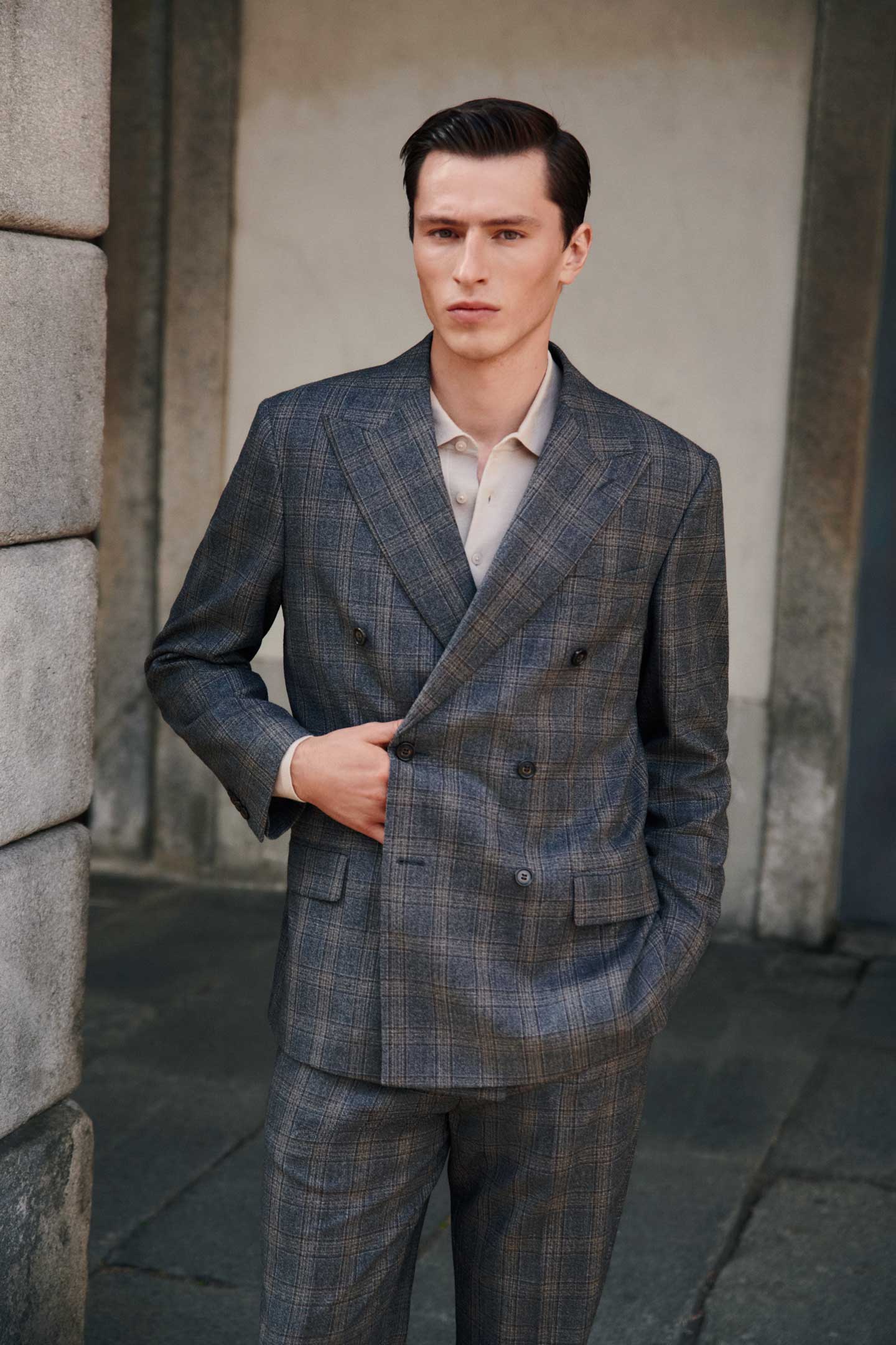 Model styled in a GANT grey patterned suit and shirt standing outdoors in front of a stone a wall.