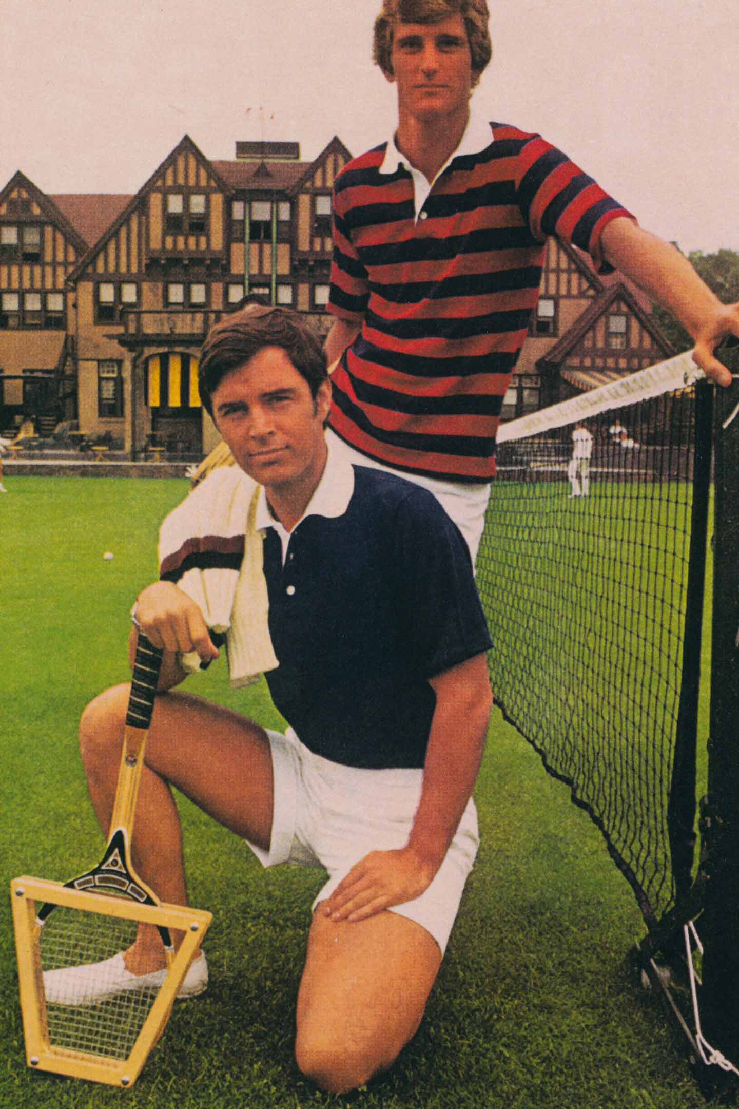 Two men in Gant tennis shirts and shorts posing by a grass court and net.