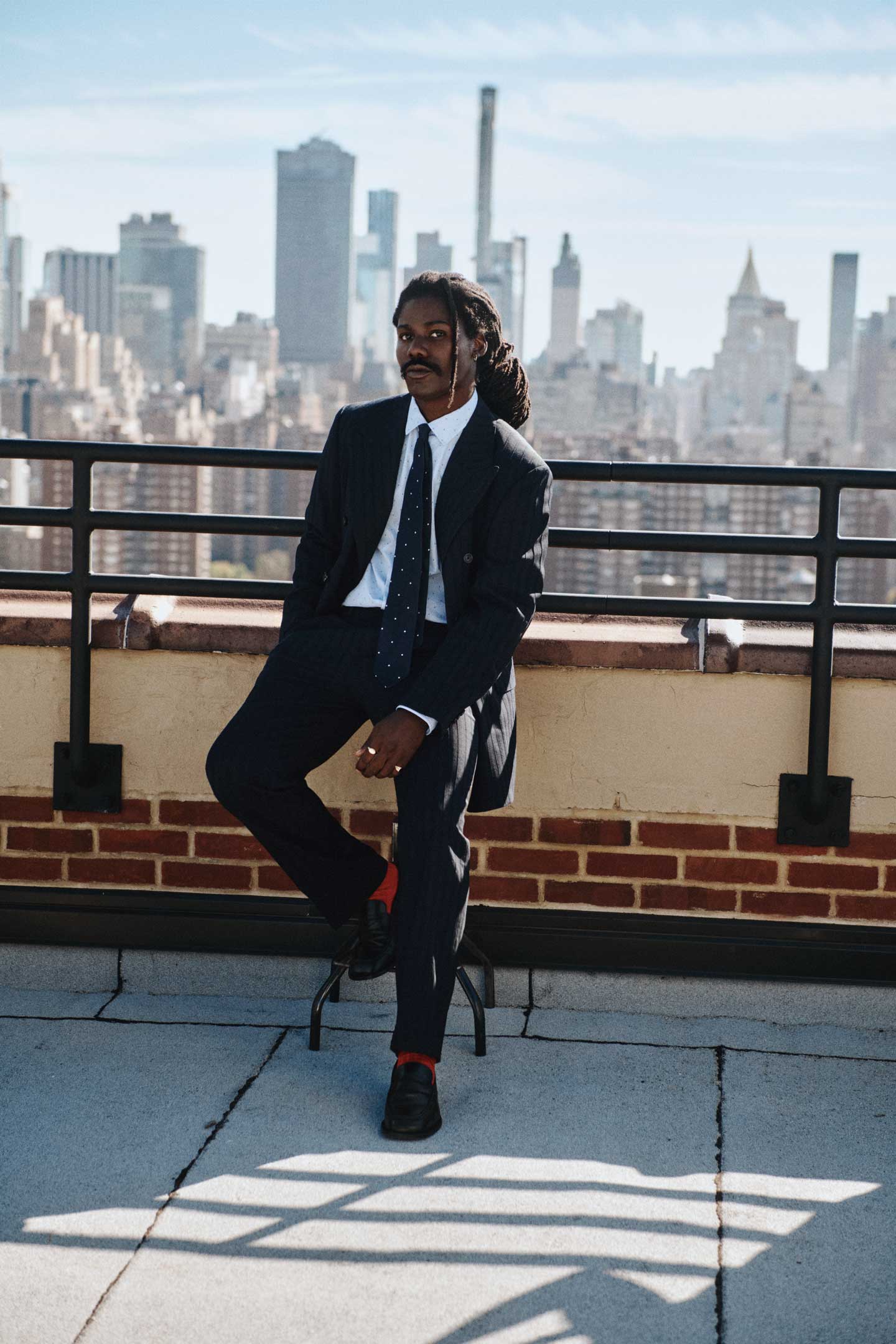 Man wearing a Gant dark suit with a white shirt and patterned tie while seated on a rooftop ledge
