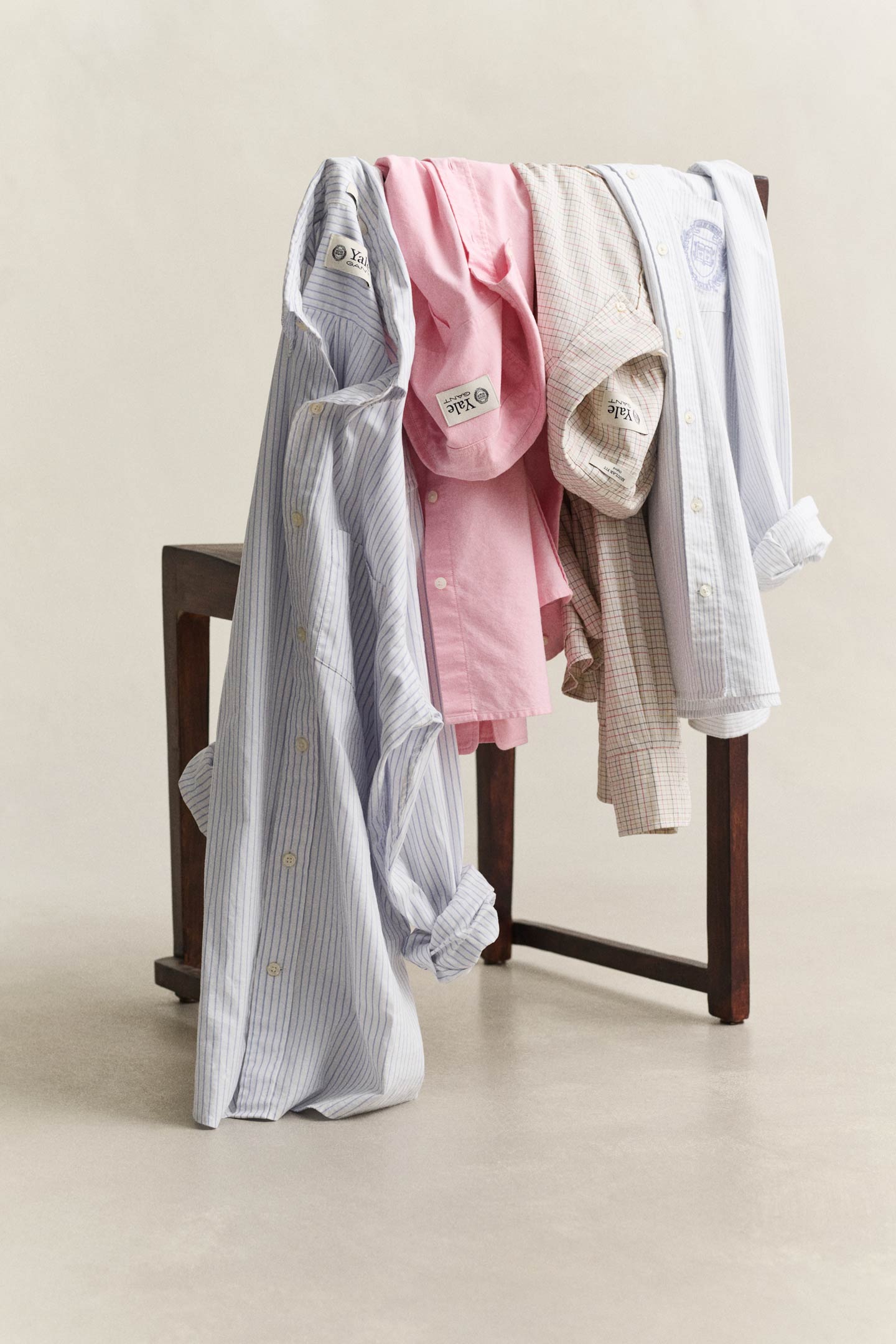 Gant Yale Oxford shirts in blue, pink and checked patterns draped over a wooden chair.