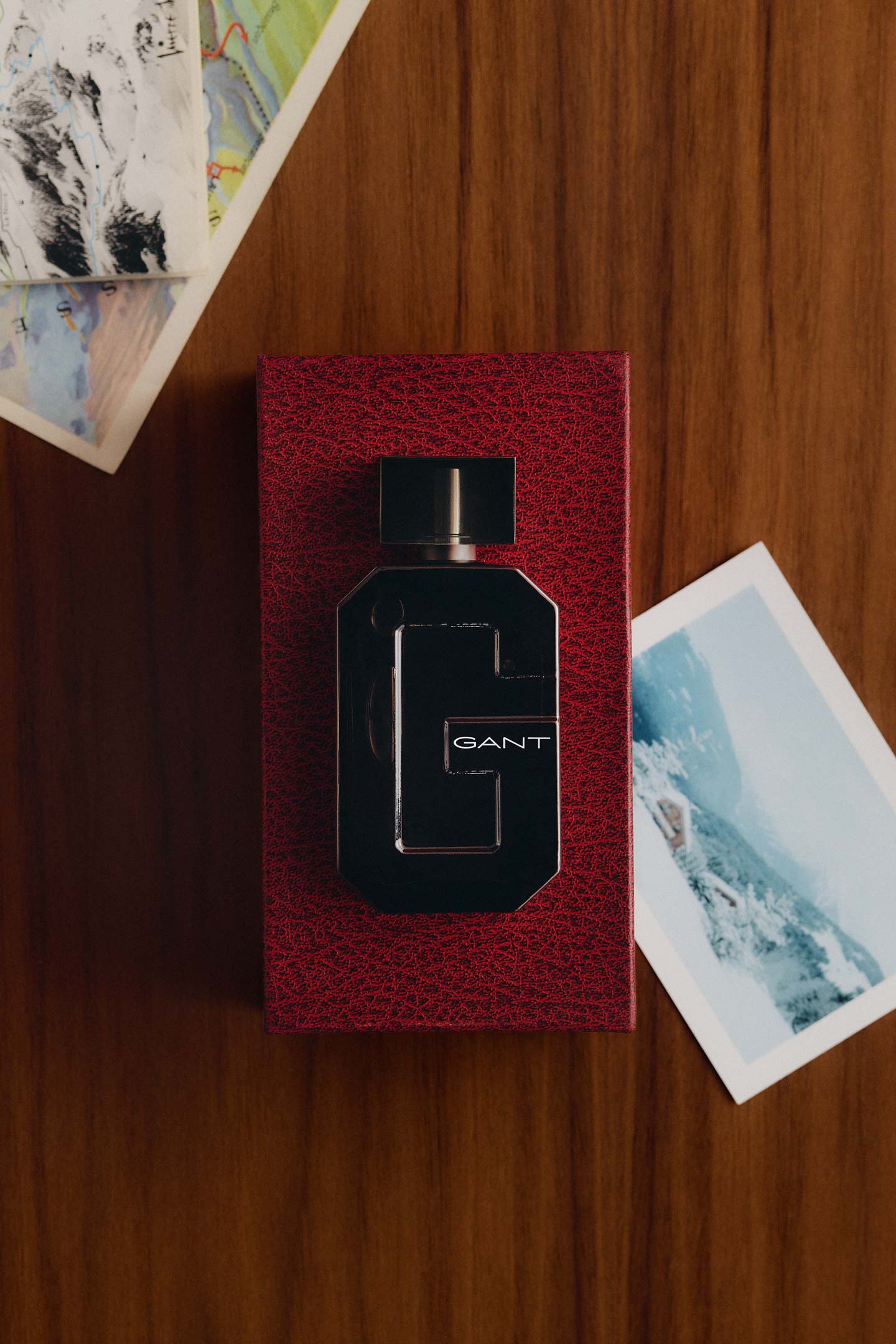 Gant fragrance bottle displayed on a red gift box against a wooden surface, surrounded by travel photographs.