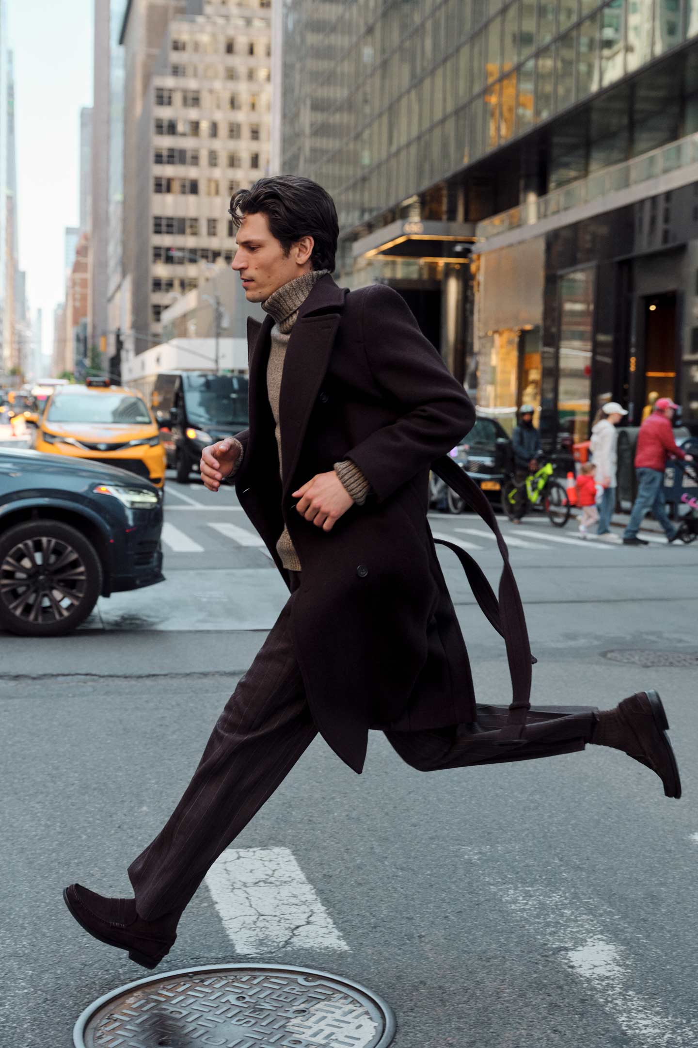 Model styled in a Gant wool overcoat worn with a roll-neck sweater and pinstripe pants, running across a road.