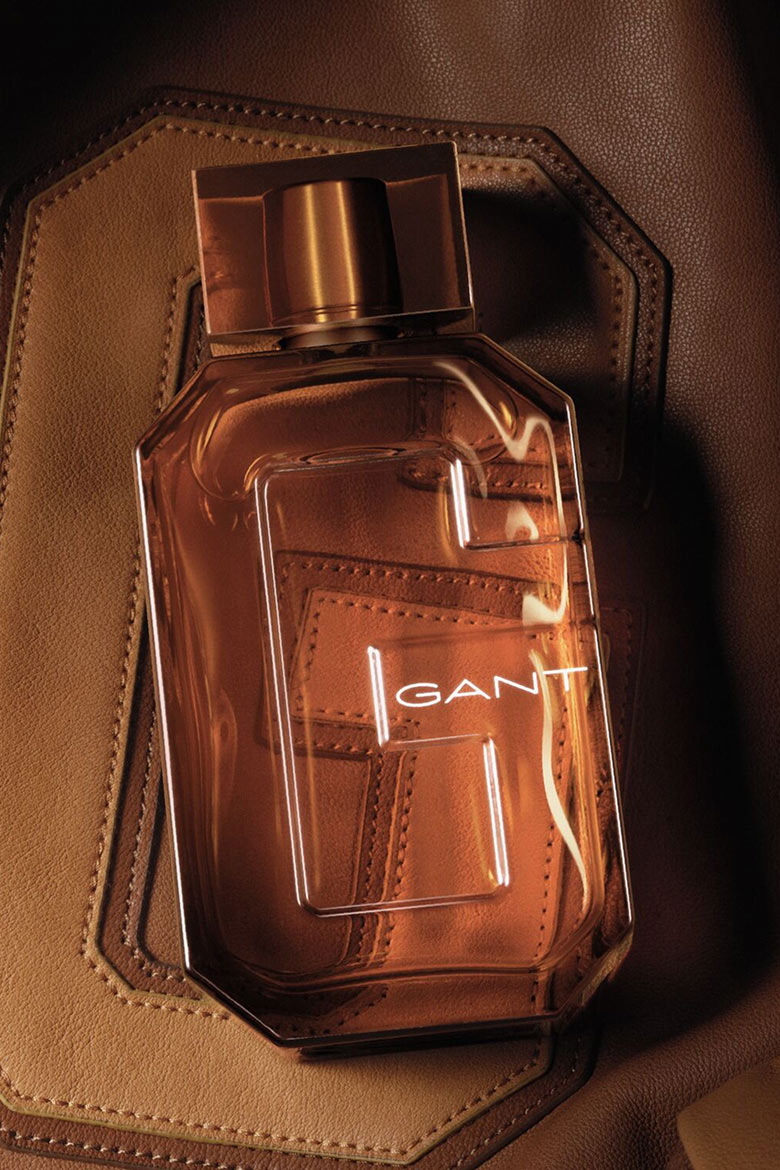 Flacon de parfum en verre brun GANT avec design G audacieux, posé sur un fond en cuir brun texturé