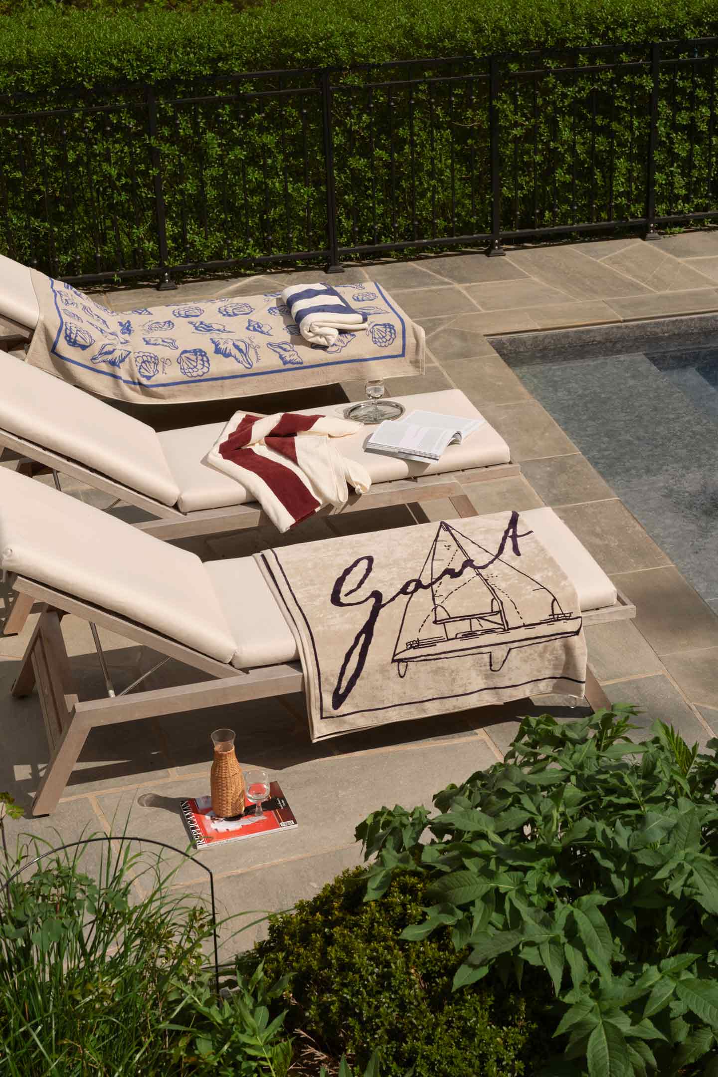 Gant beach towels displayed on poolside loungers beside a swimming pool.
