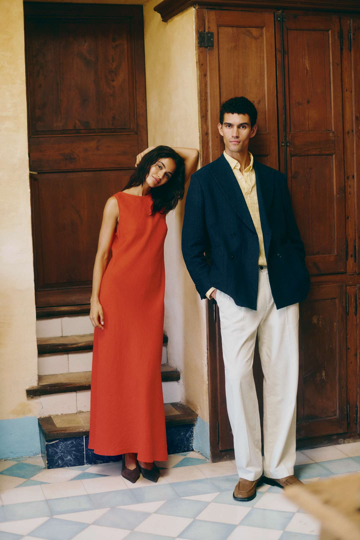 Persons wearing Gant occasion clothing, including a long red dress and a navy blazer with light trousers, standing indoors