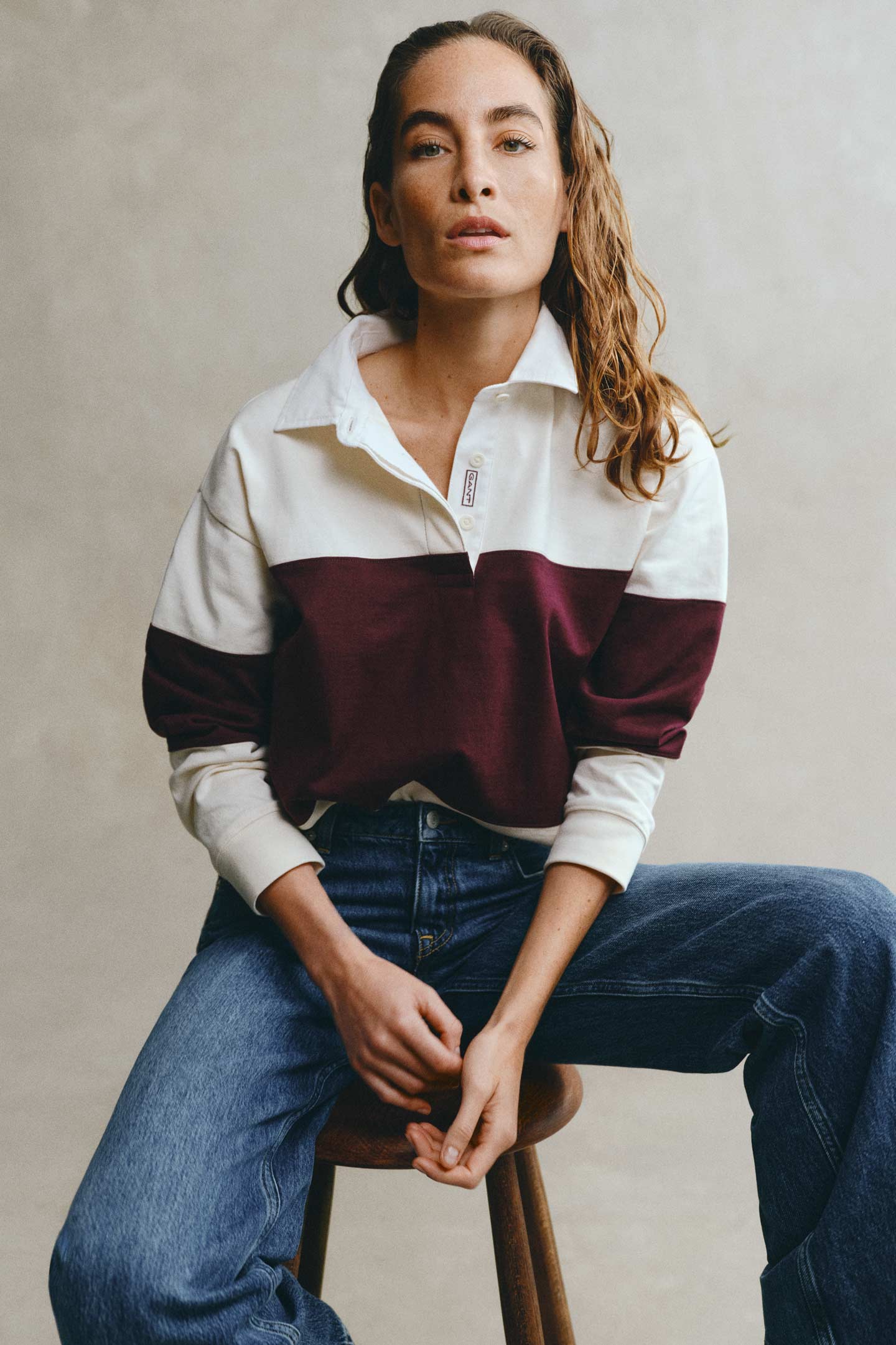 Model styled in a GANT color-blocked rugger layered over a shirt with jeans sitting in front of a grey backdrop.