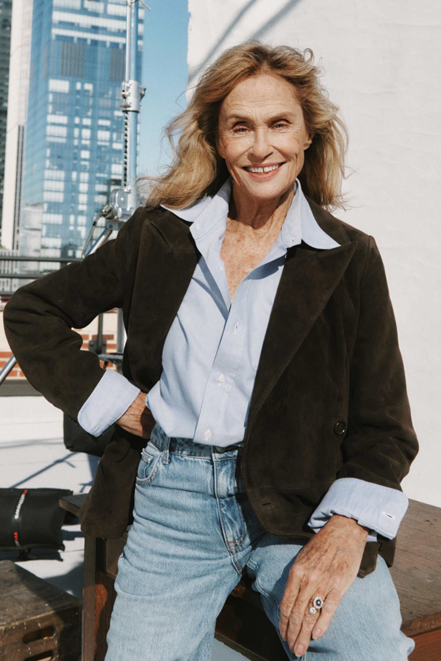 Woman wearing a Gant suede jacket, light blue shirt and jeans sitting on a rooftop set
