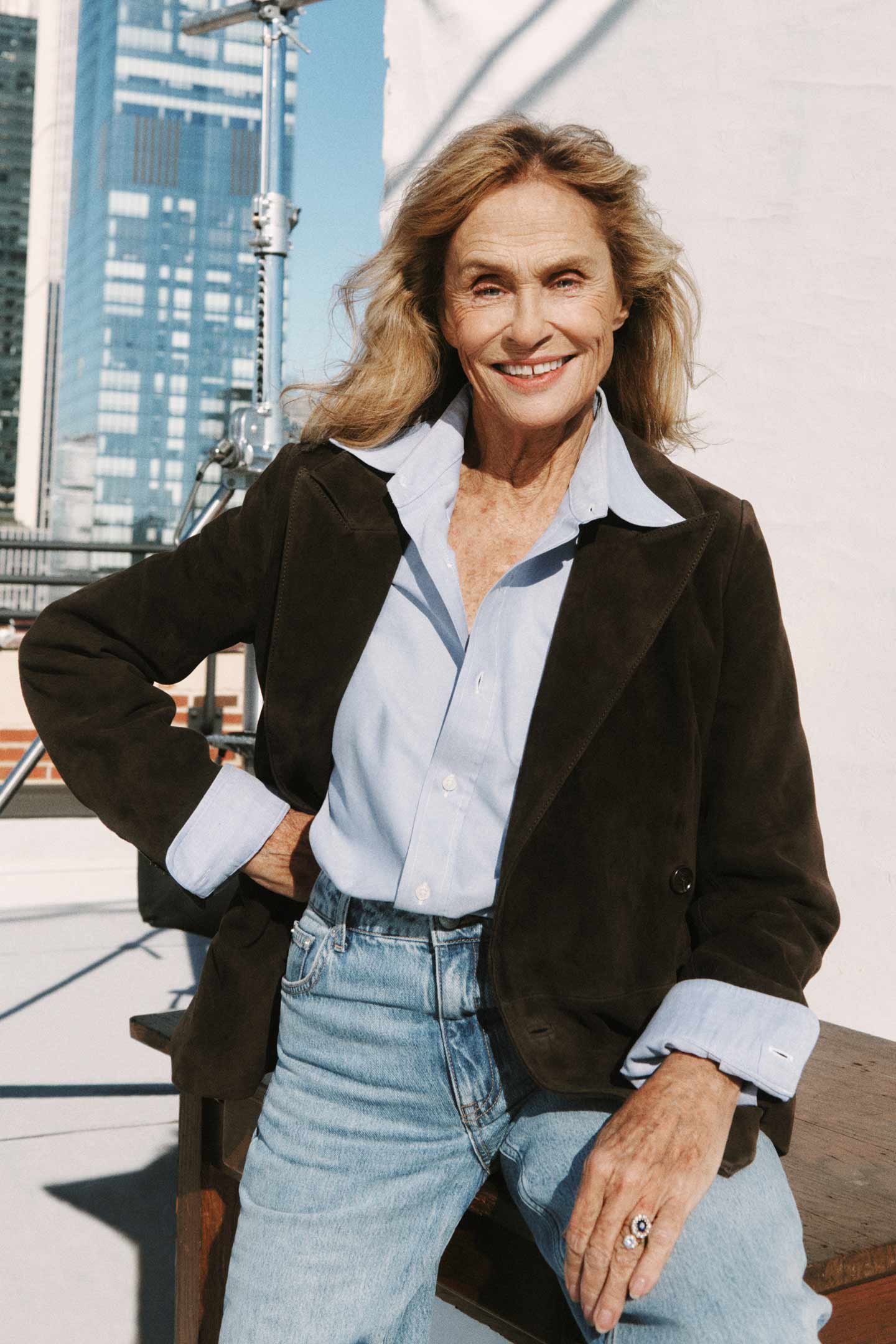 Woman wearing a Gant suede jacket, light blue shirt and jeans sitting on a rooftop set