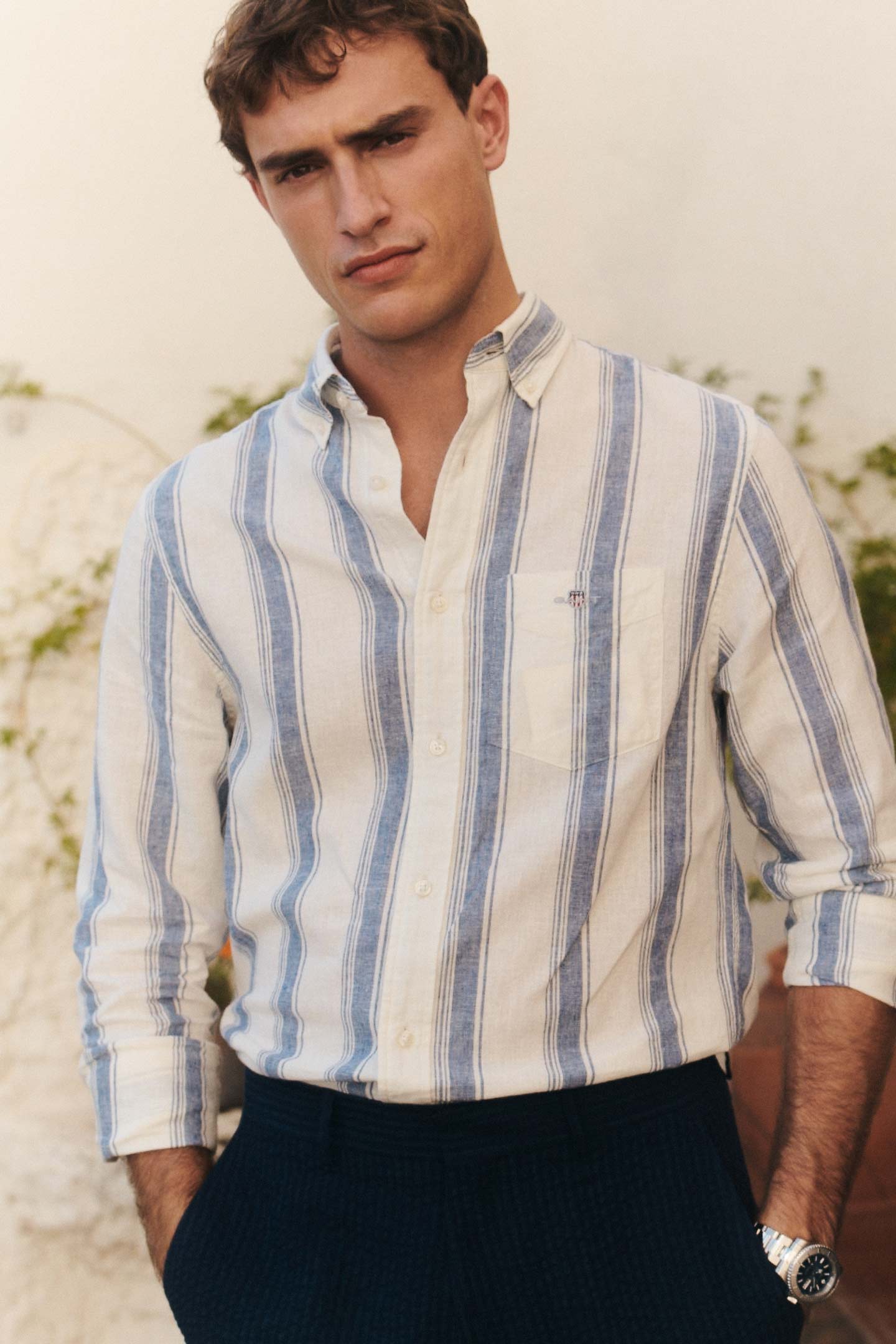 Man wearing a Gant striped button‑down shirt with dark trousers in an outdoor setting.