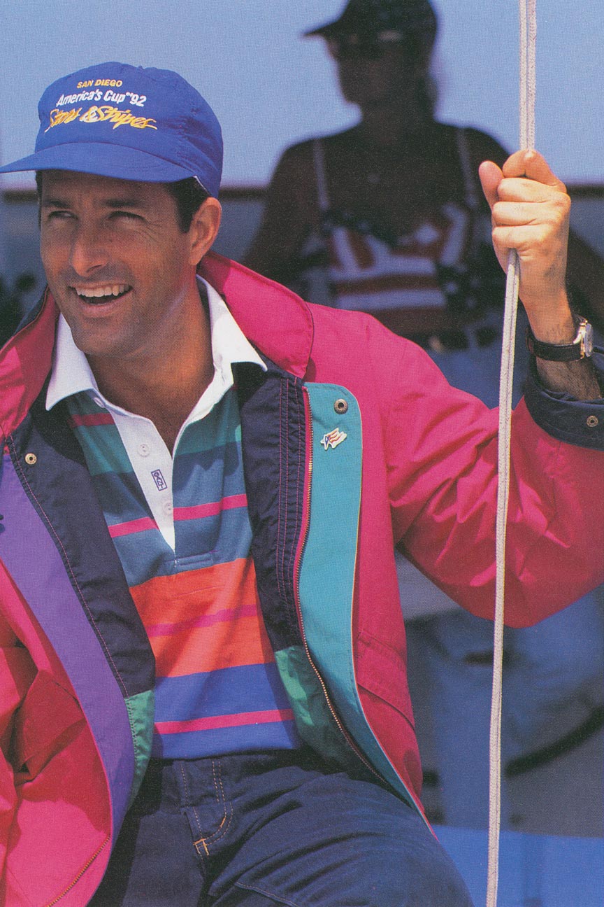 Uomo che indossa una giacca da vela Gant brillante sopra una maglia da rugby a righe su una barca.