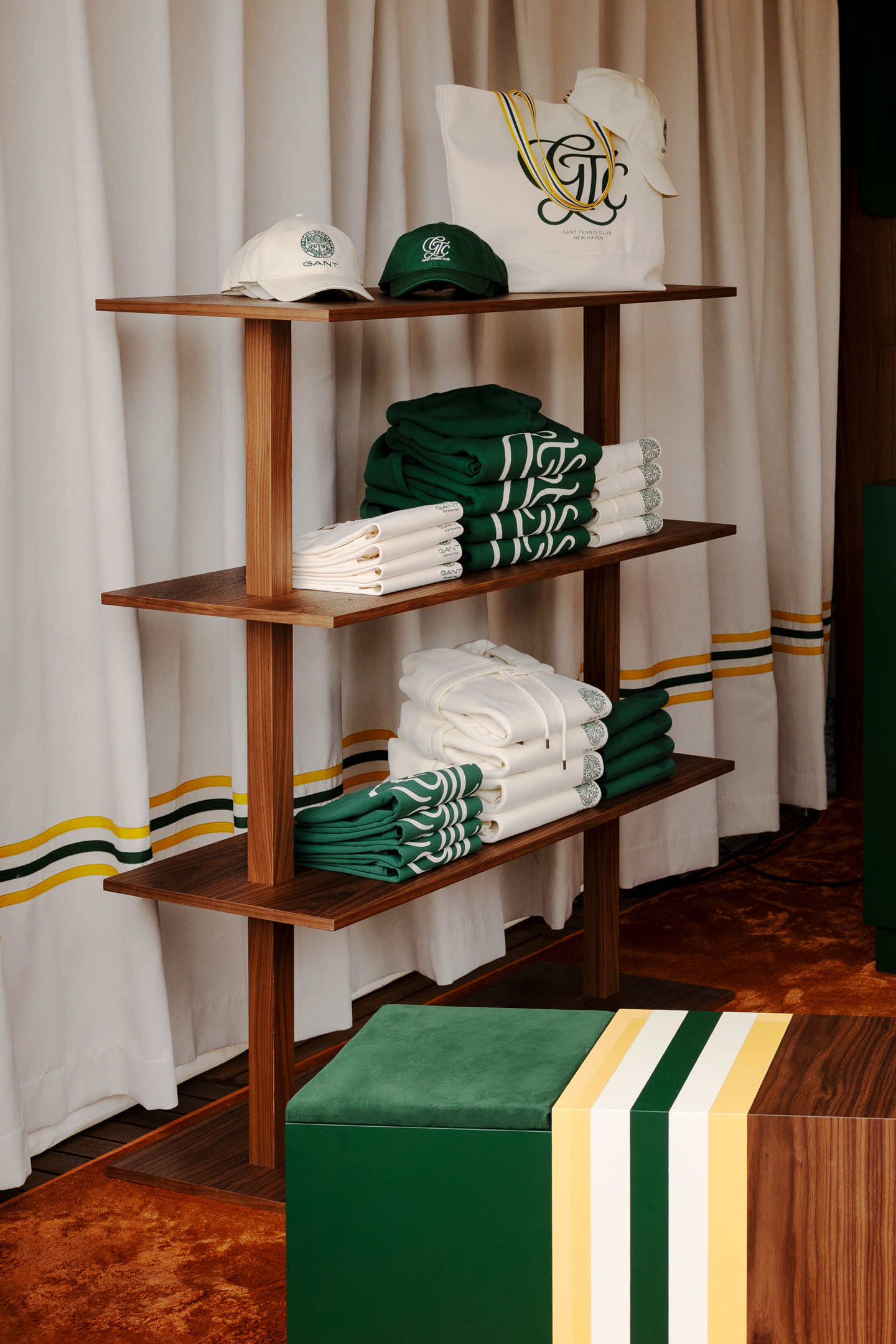 Folded green and white Gant apparel displayed on a wooden shelf with matching caps and tote bag.