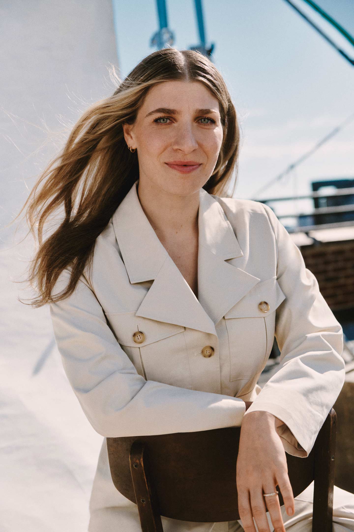 Woman wearing a Gant cream tailored jacket while seated outdoors with wind blowing through her hair