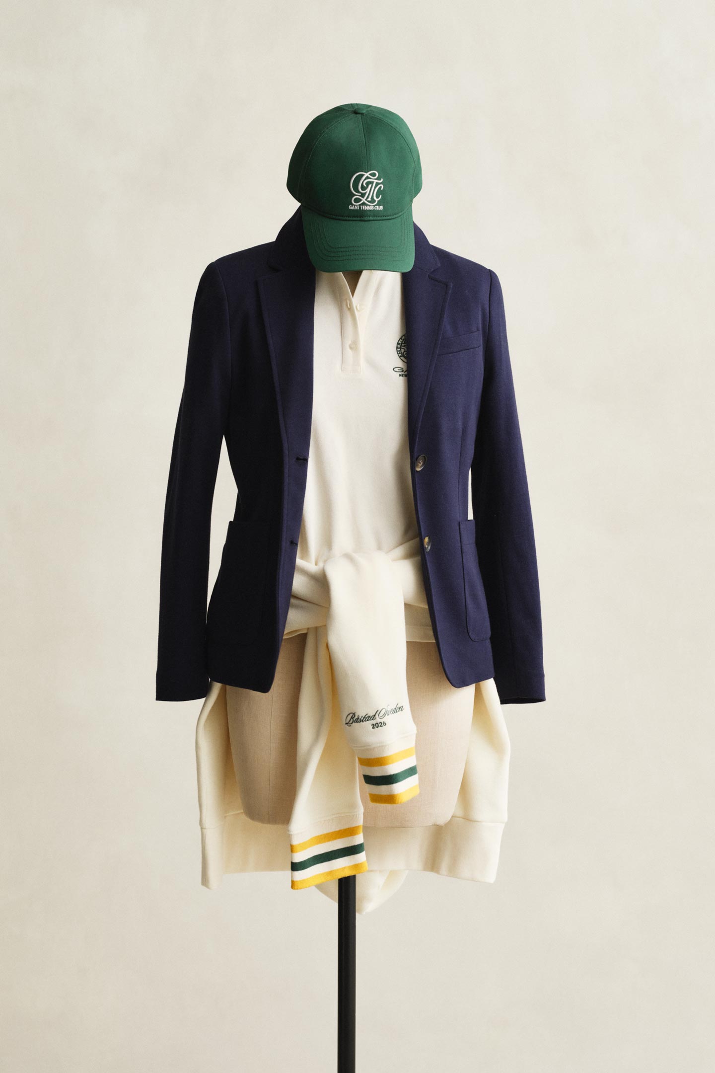 Gant navy blazer layered over a polo shirt with a sweater tied at the waist and a cap displayed on a mannequin.