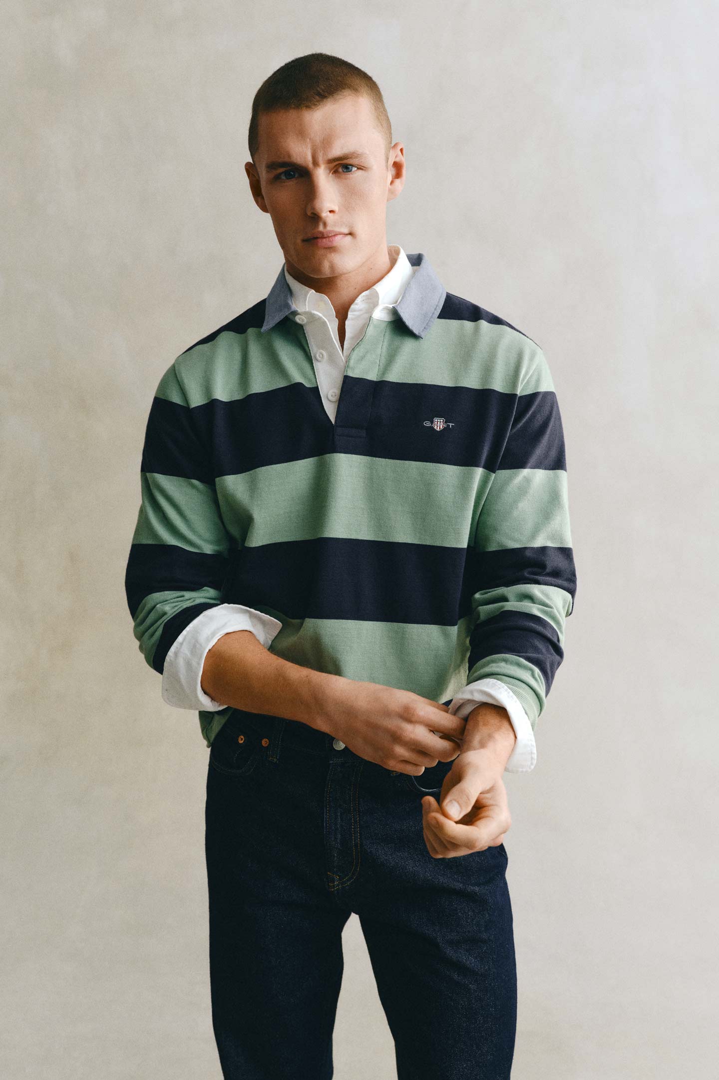 Model styled in a GANT striped rugger paired with dark denim jeans in front of a grey backdrop.