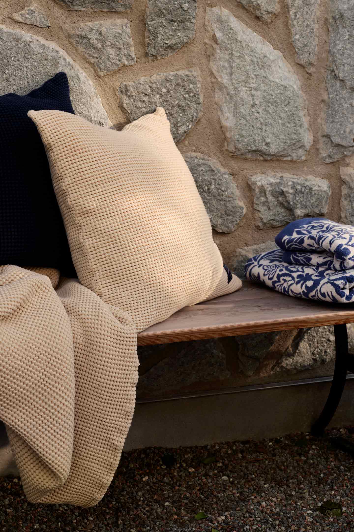 Gant knit cushion and throw blanket styled on a wooden bench.