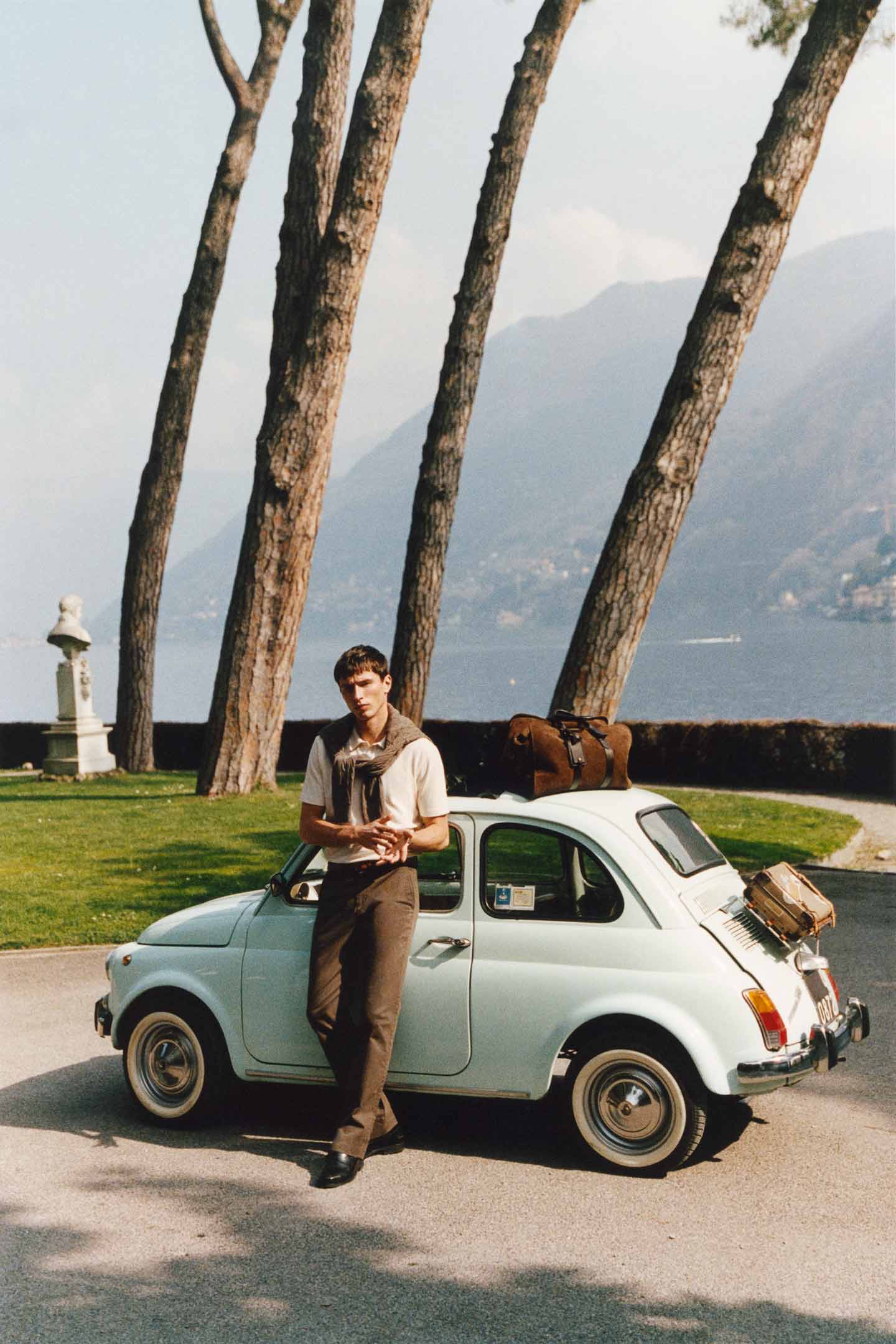 Model styled in GANT polo shirt paired with brown pants standing in front of a vintage car and palm trees.