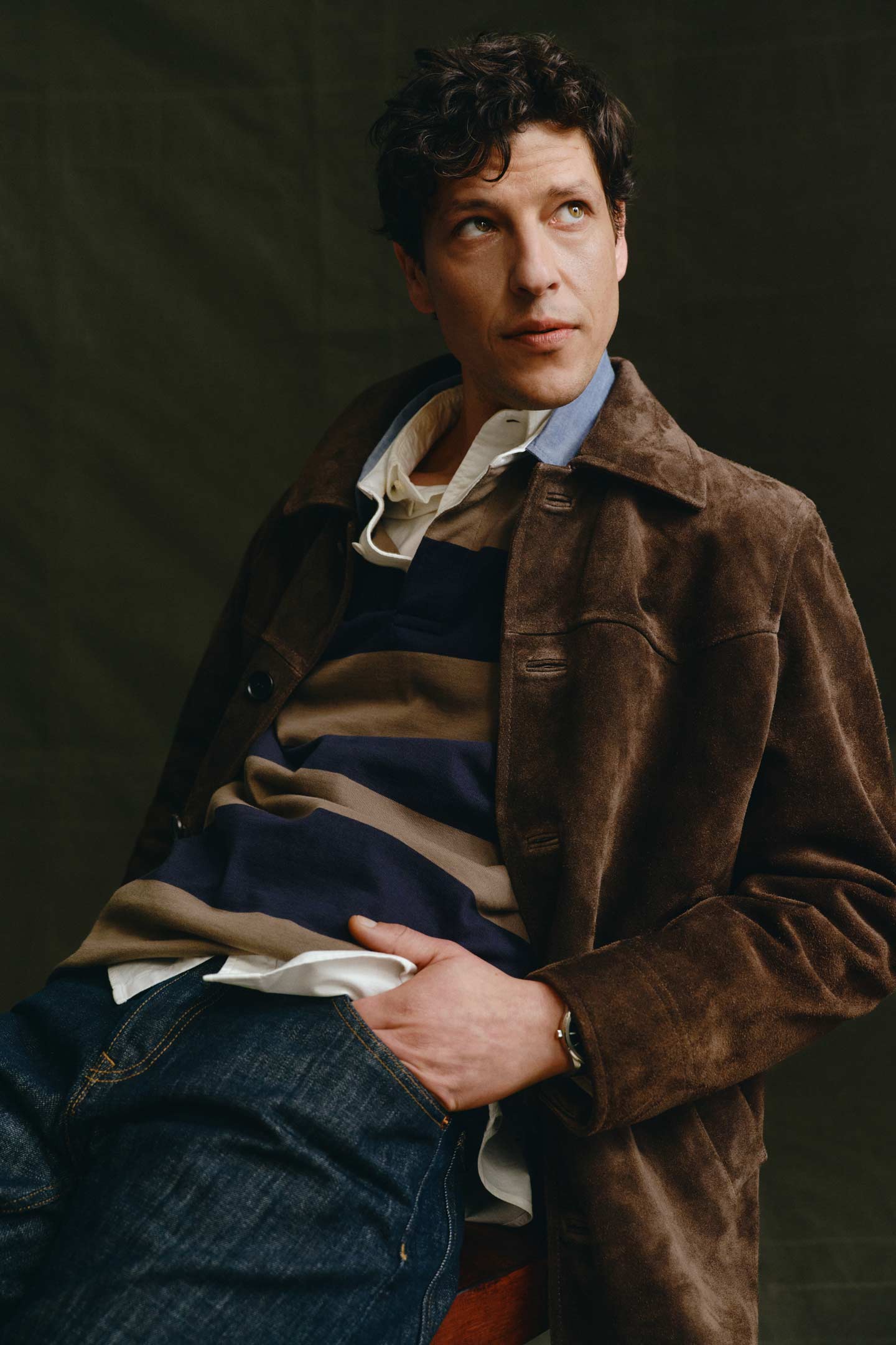 Model styled in a Gant suede jacket layered over a striped rugby shirt and jeans, seated in a studio setting.