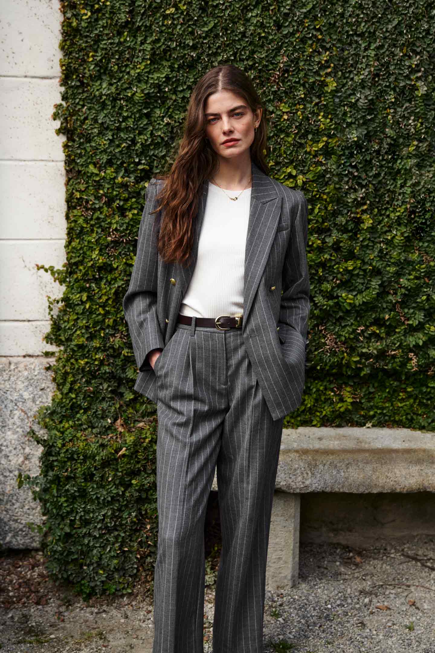 Model styled in a GANT grey stripe tailored suit with a white top standing in front of greenery.