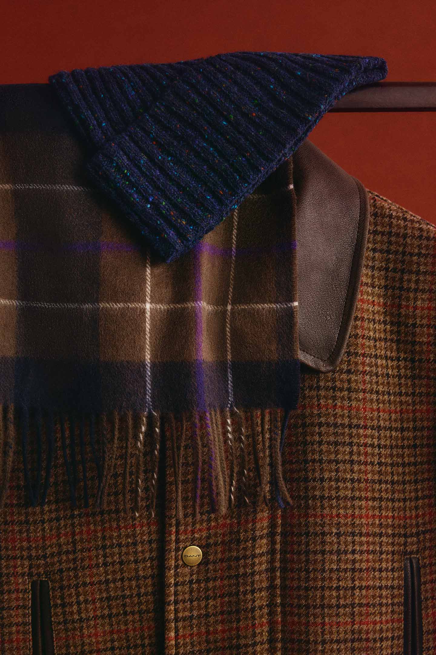 Brown checked Gant jacket with a navy plaid scarf and blue rib-knit beanie draped over the shoulders.