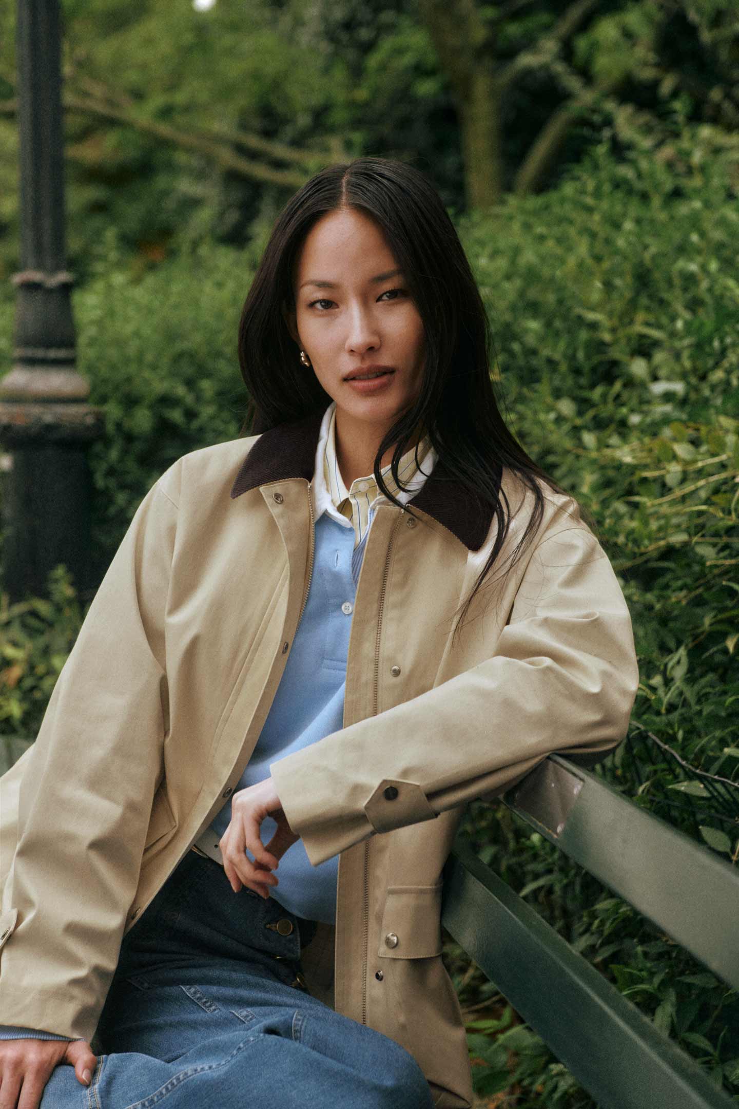 Person wearing a Gant beige jacket over a blue shirt, seated on a park bench.