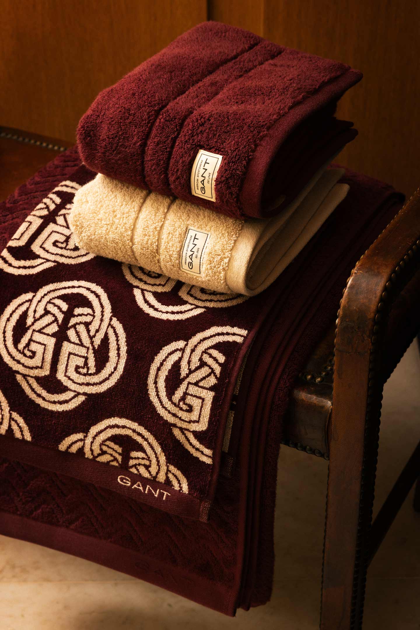Gant patterned bath towel with folded Gant towels arranged on a wooden chair.