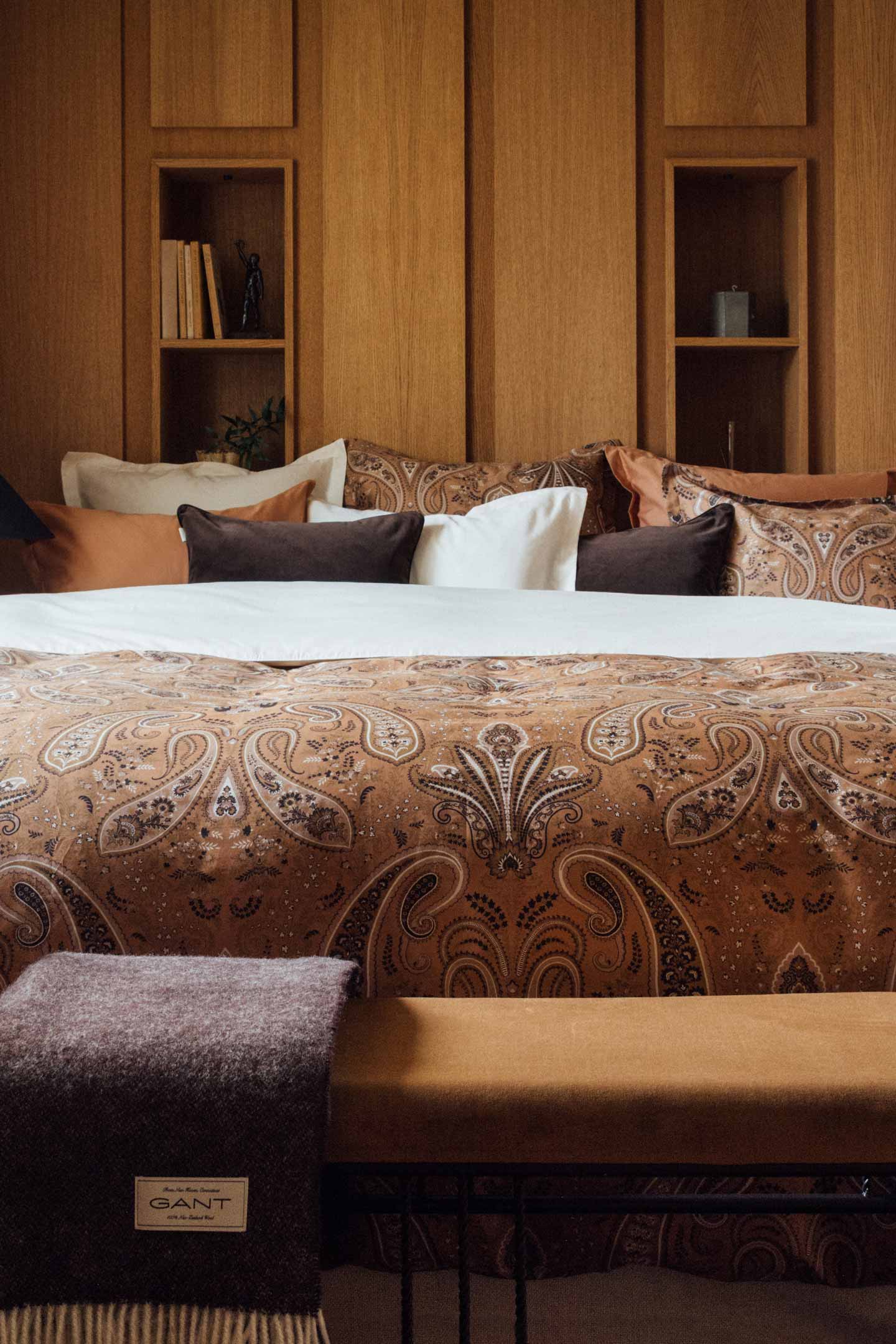 Gant paisley bedding styled on a bed with matching pillows in a wood-panelled bedroom.