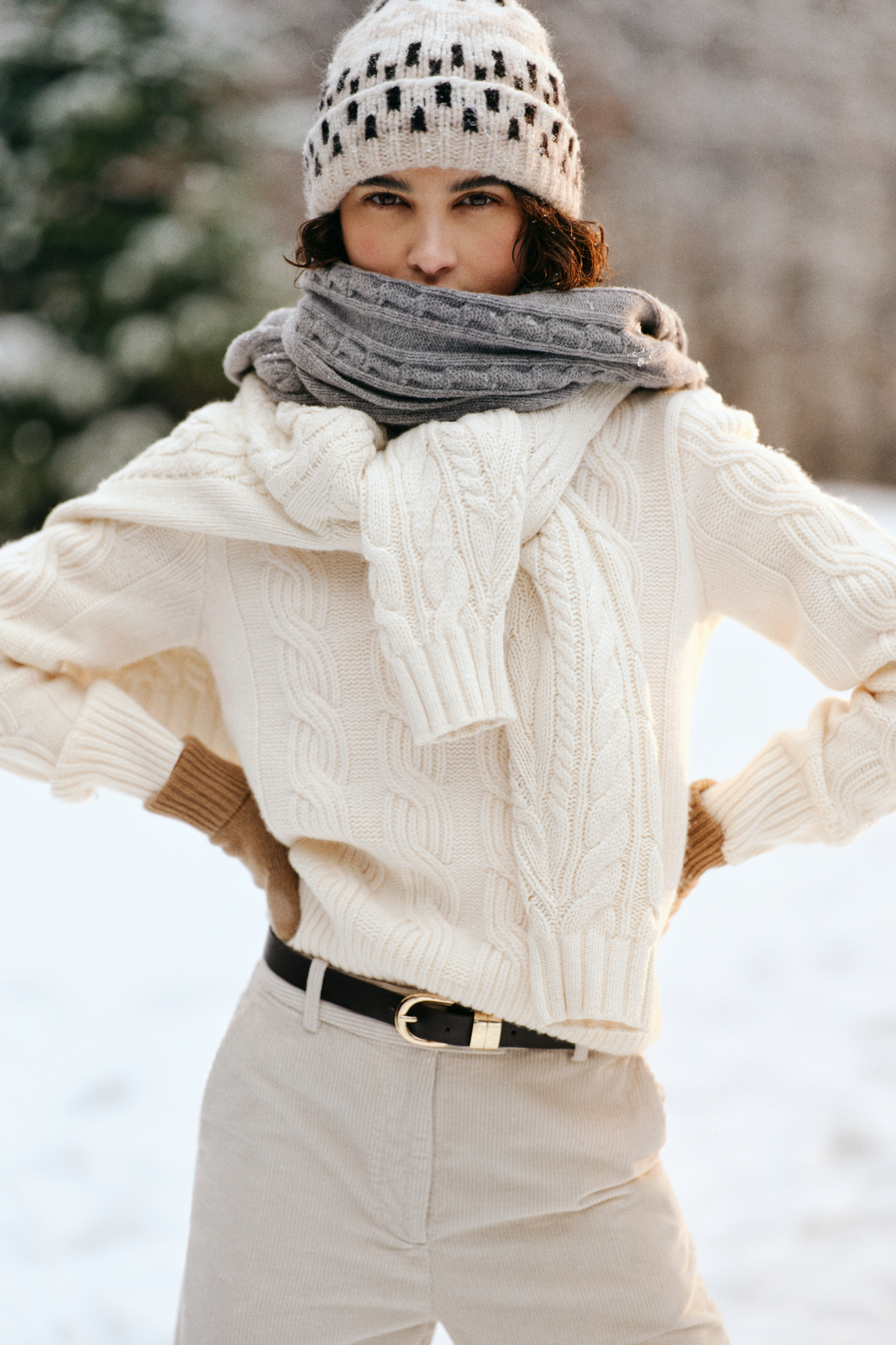 Model styled in a Gant cable-knit sweater paired with a scarf, beanie and corduroy pants in a snowy setting.