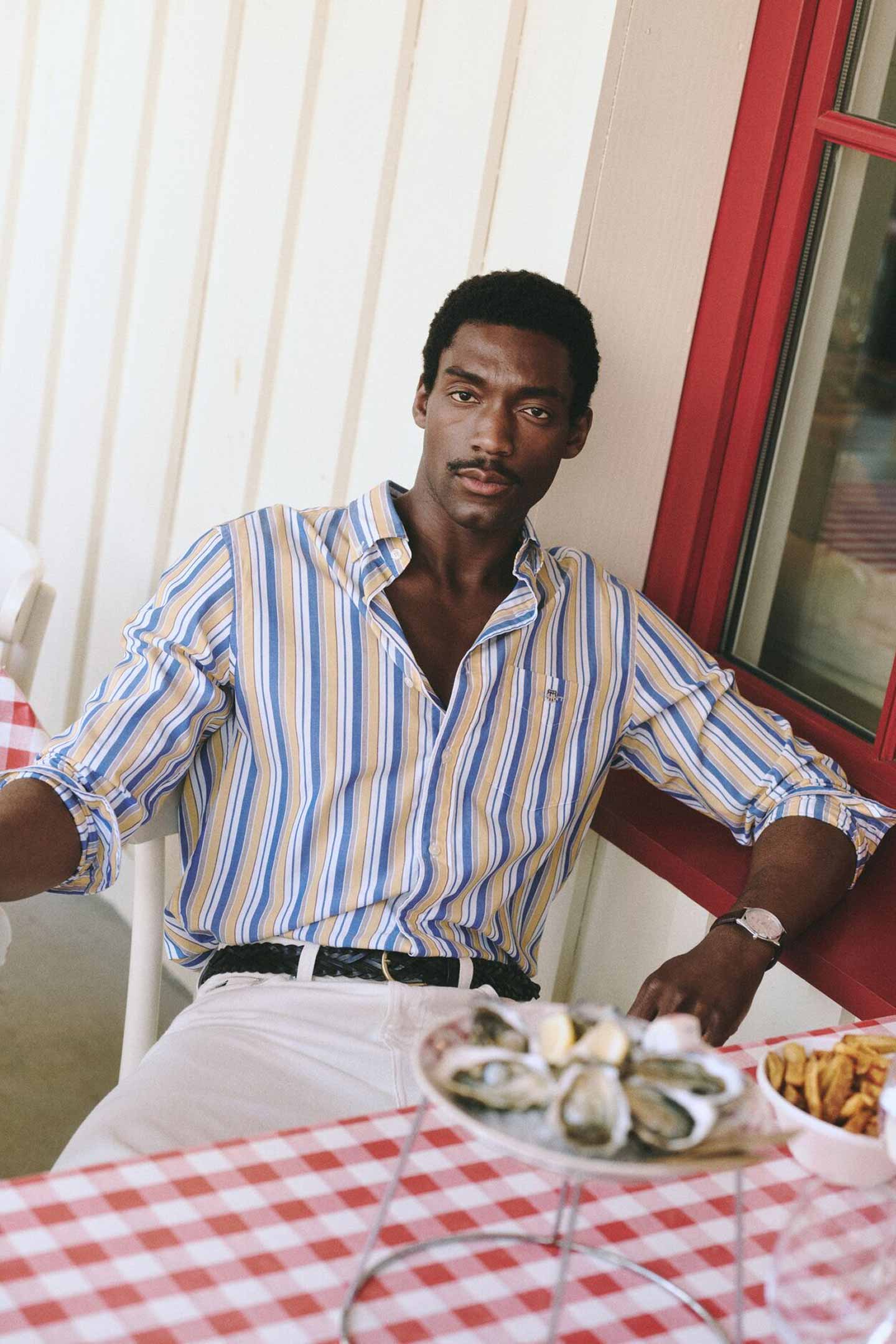 Gant striped button-down shirt worn by a person seated at an outdoor table with seafood and drinks.