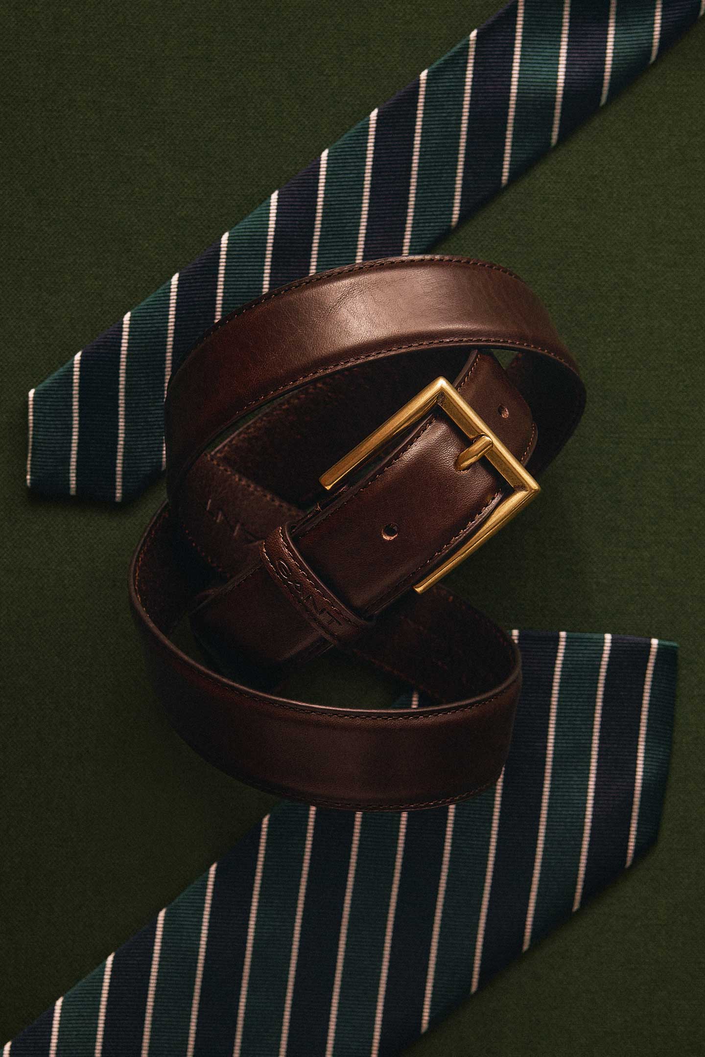 Brown Gant leather belt with a gold-tone buckle displayed alongside navy striped tie.