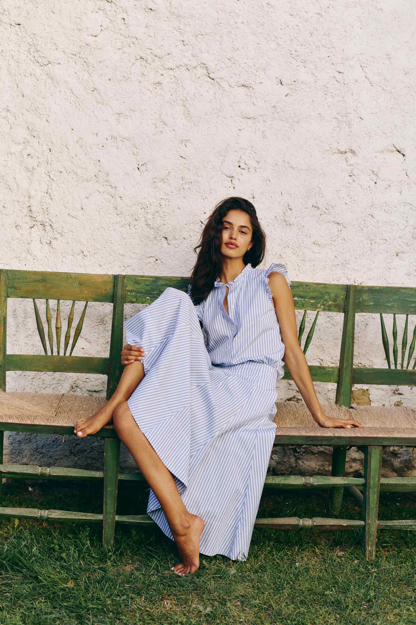 Woman wearing a Gant blue striped dress seated on a wooden bench outdoors.