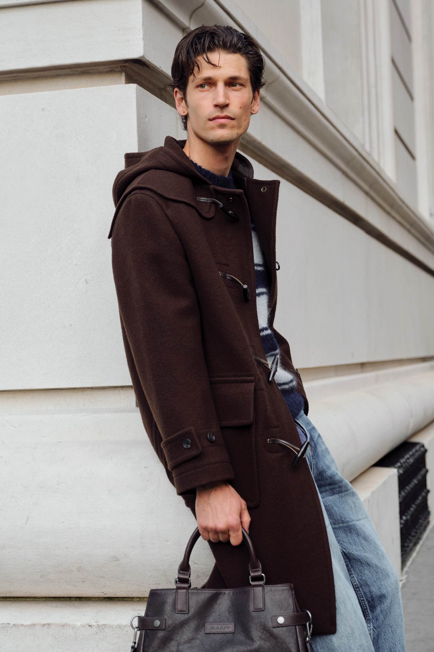 Model styled in a Gant duffle coat layered over a patterned knit sweater and jeans, holding a leather bag.