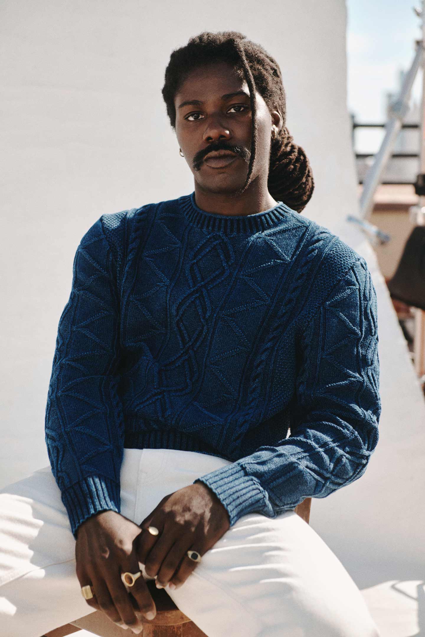 Man wearing Gant blue cable‑knit sweater paired with white trousers in an outdoor setting