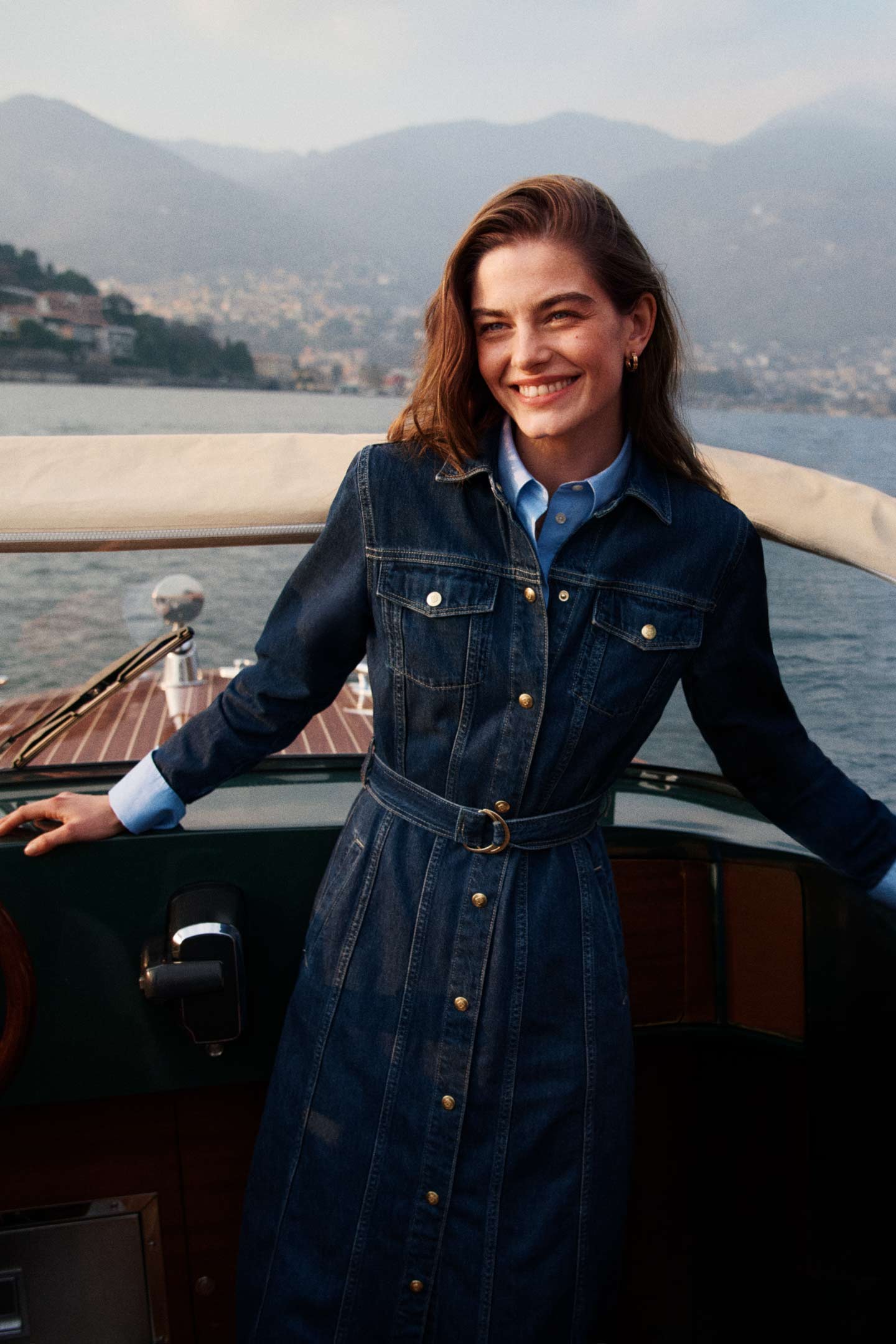 Model styled in a GANT denim shirt dress standing on a boat by the water.