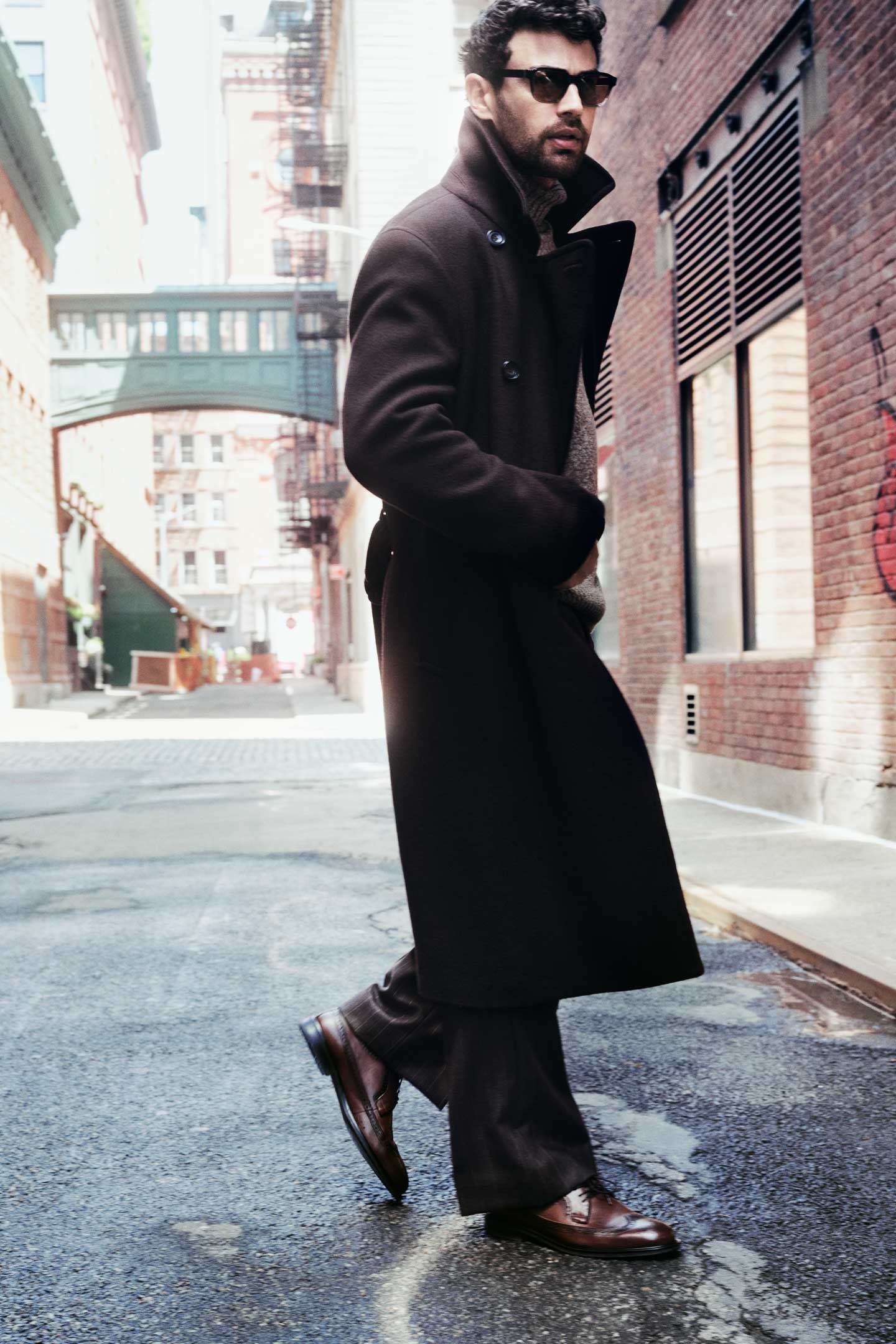 Actor Theo James styled in a GANT long wool coat, paired with dark trousers, knitwear, and leather shoes in a city setting.