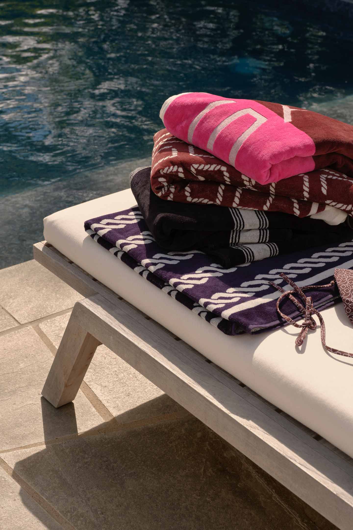 Gant beach towels stacked on a lounger beside a swimming pool.